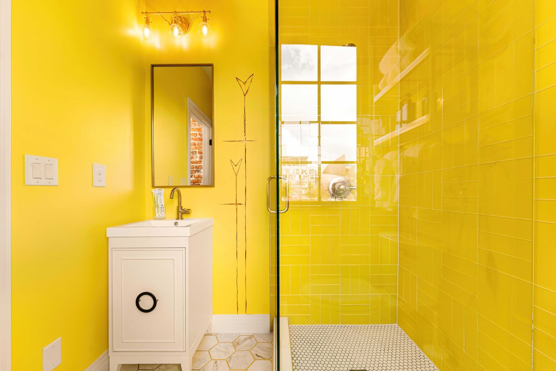 Bright yellow bathroom with a white vanity, mirror, window, and tiled shower area