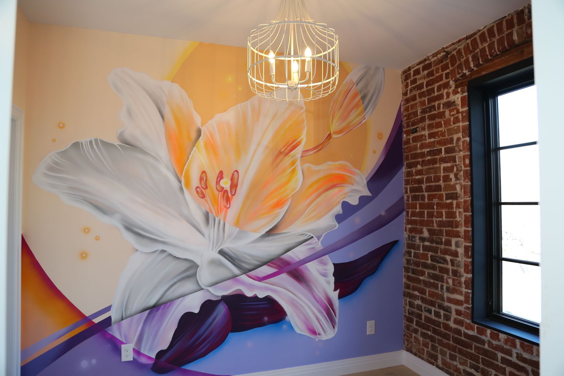 Colorful flower mural on a wall in a room with exposed brick and a black-framed window