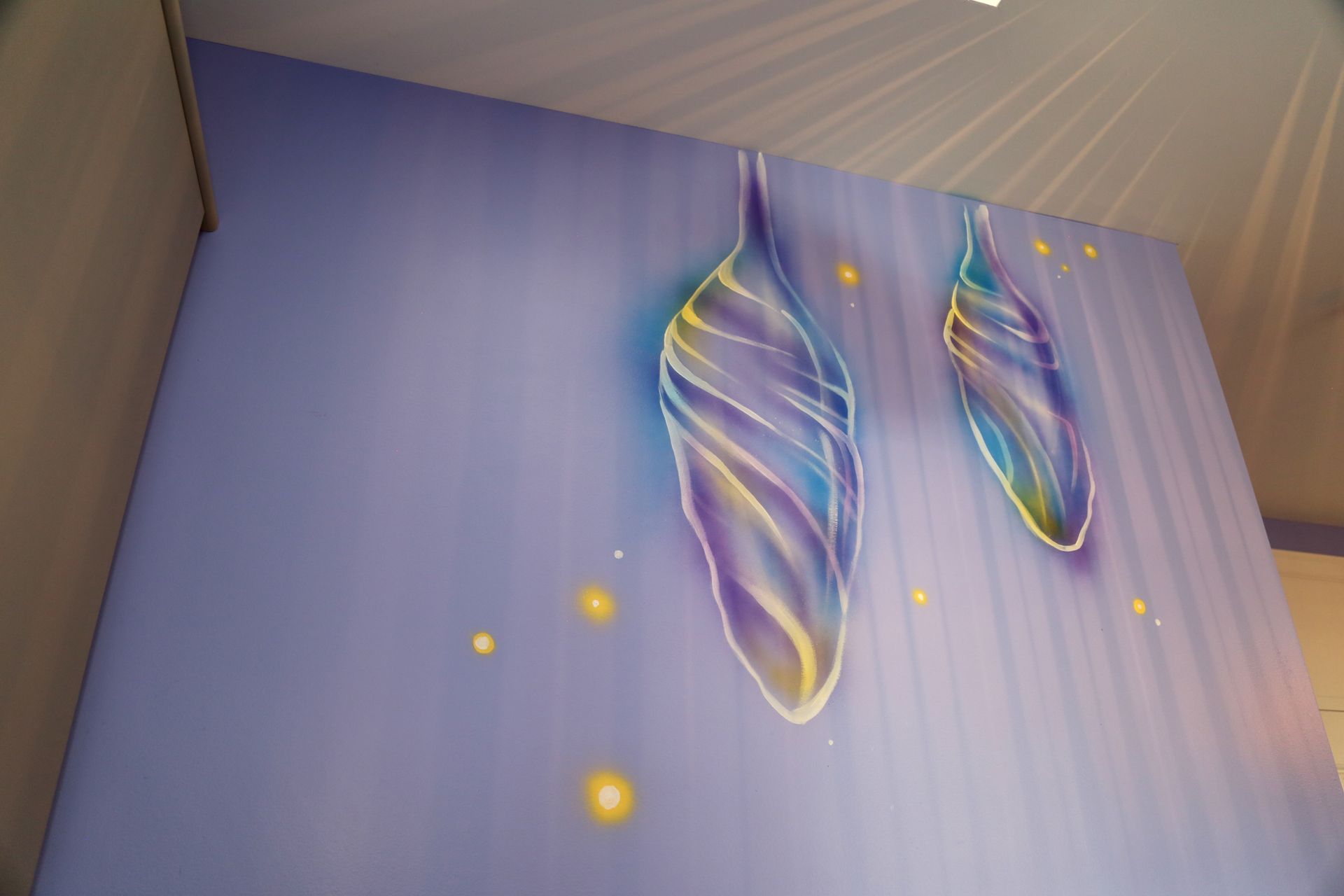 Abstract wall art with two colorful, wing-like hanging sculptures on a purple wall and small glowing dots