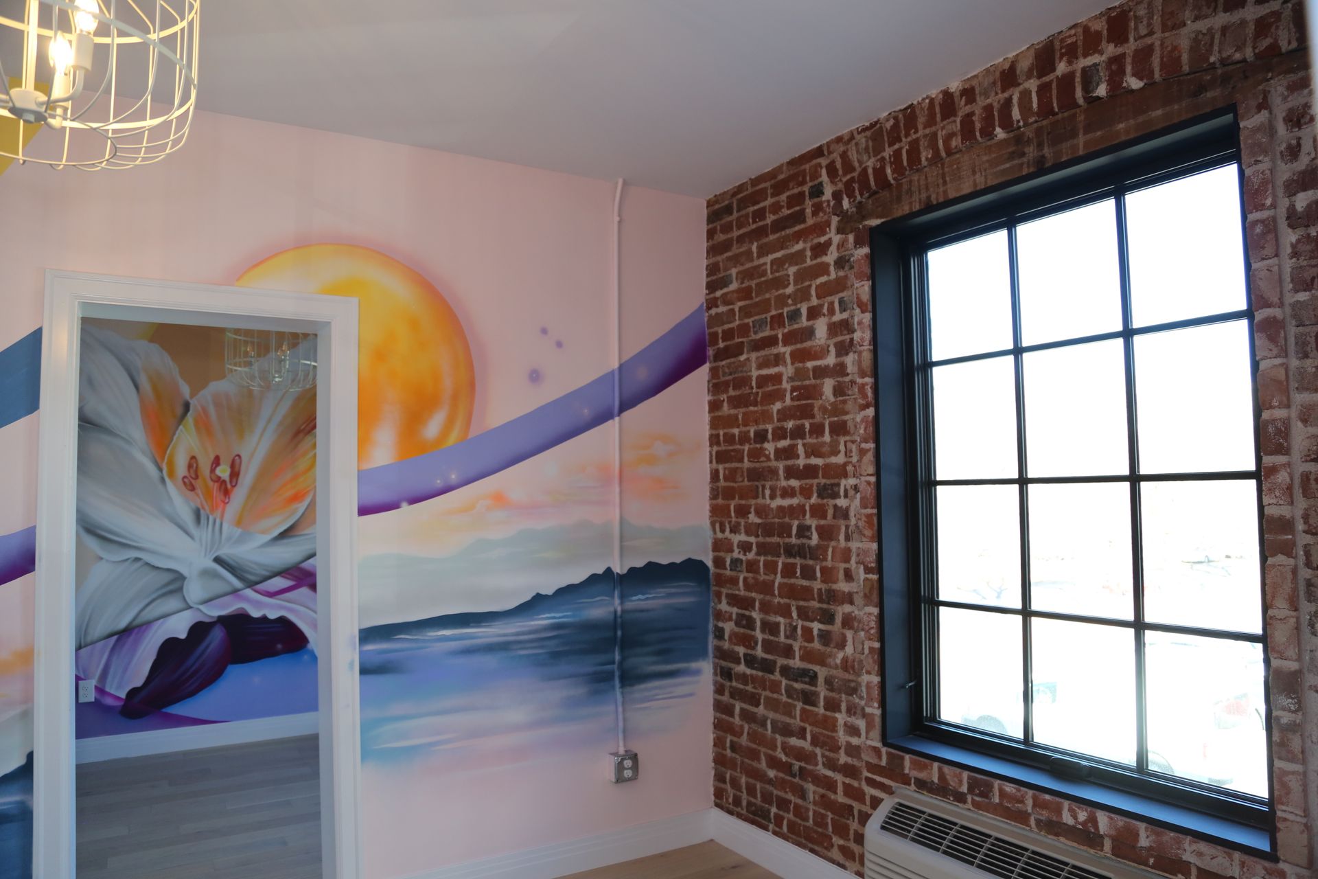Artistic mural on a pink wall beside a brick-framed window in a bright room