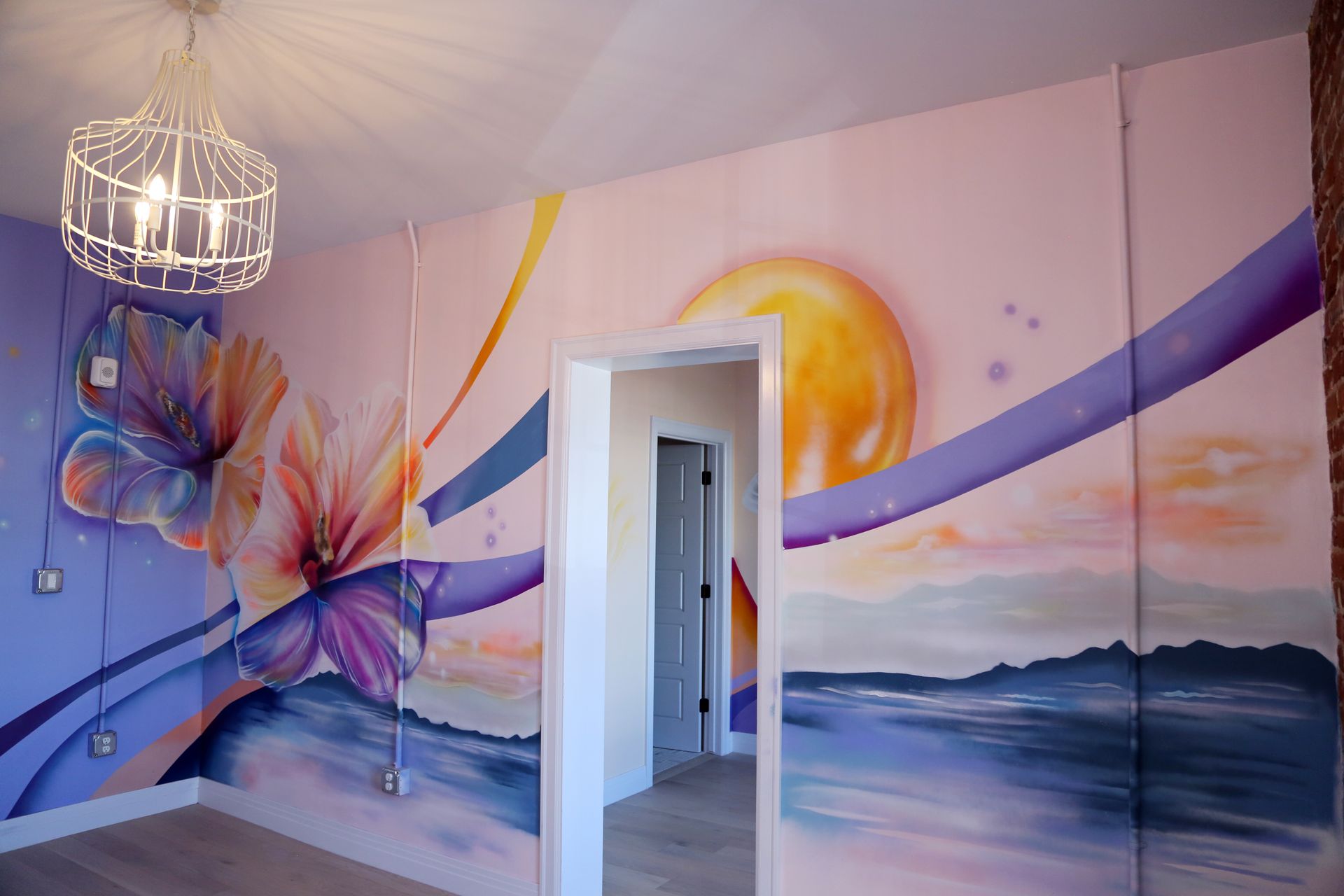 Colorful mural on a room wall with abstract flowers, sun, waves, and a doorway.