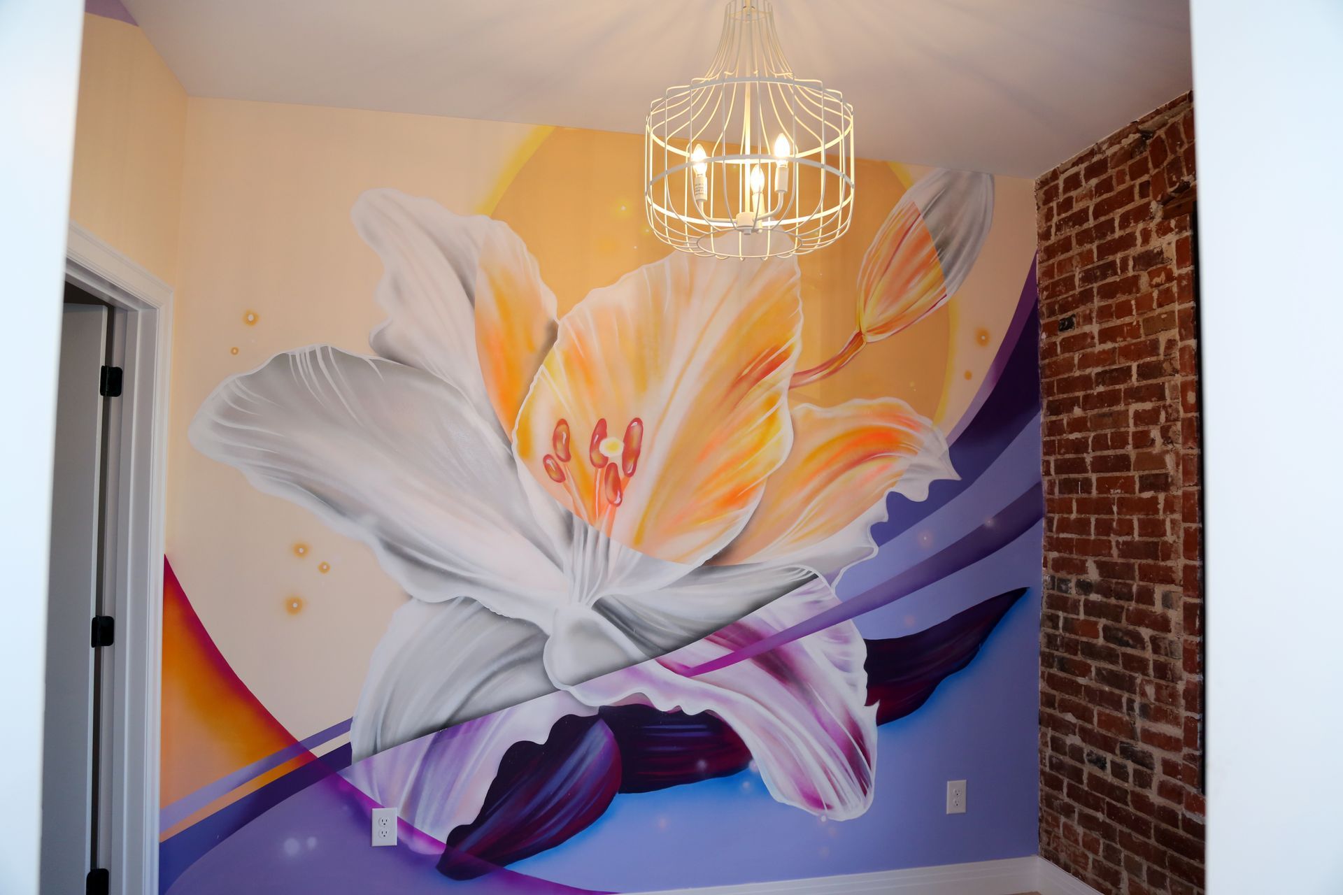 Mural of a white bird with orange and purple accents on a bedroom wall beneath a chandelier