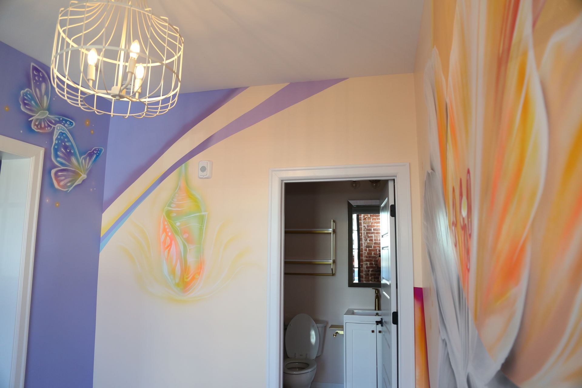 Colorful hallway with pastel wall murals, a hanging light fixture, and an open doorway to a bathroom.