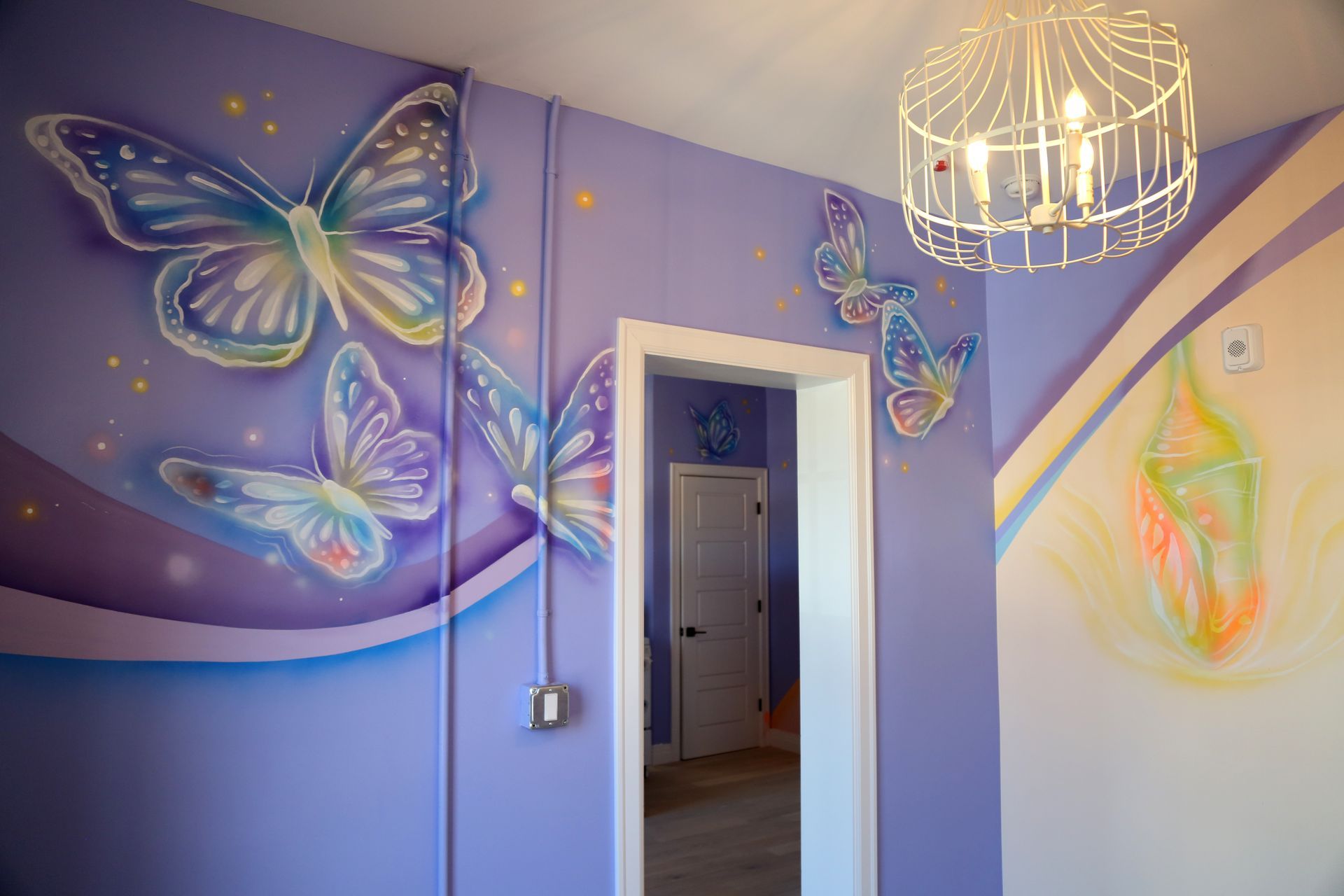 Purple hallway with large butterfly murals, pastel wall art, and a hanging ceiling light
