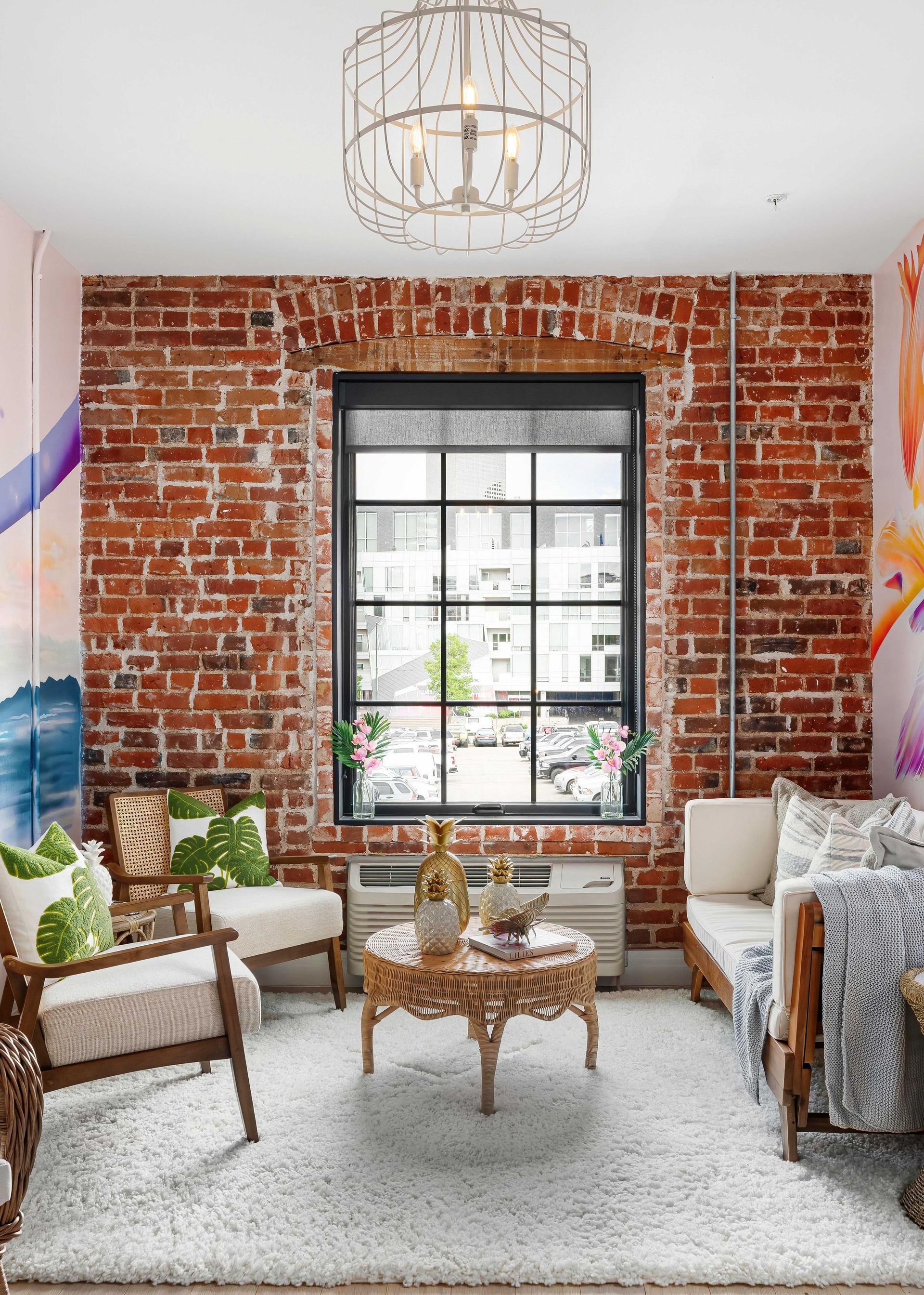 Cozy living room with exposed brick wall, large window, white sofa, plants, and round coffee table