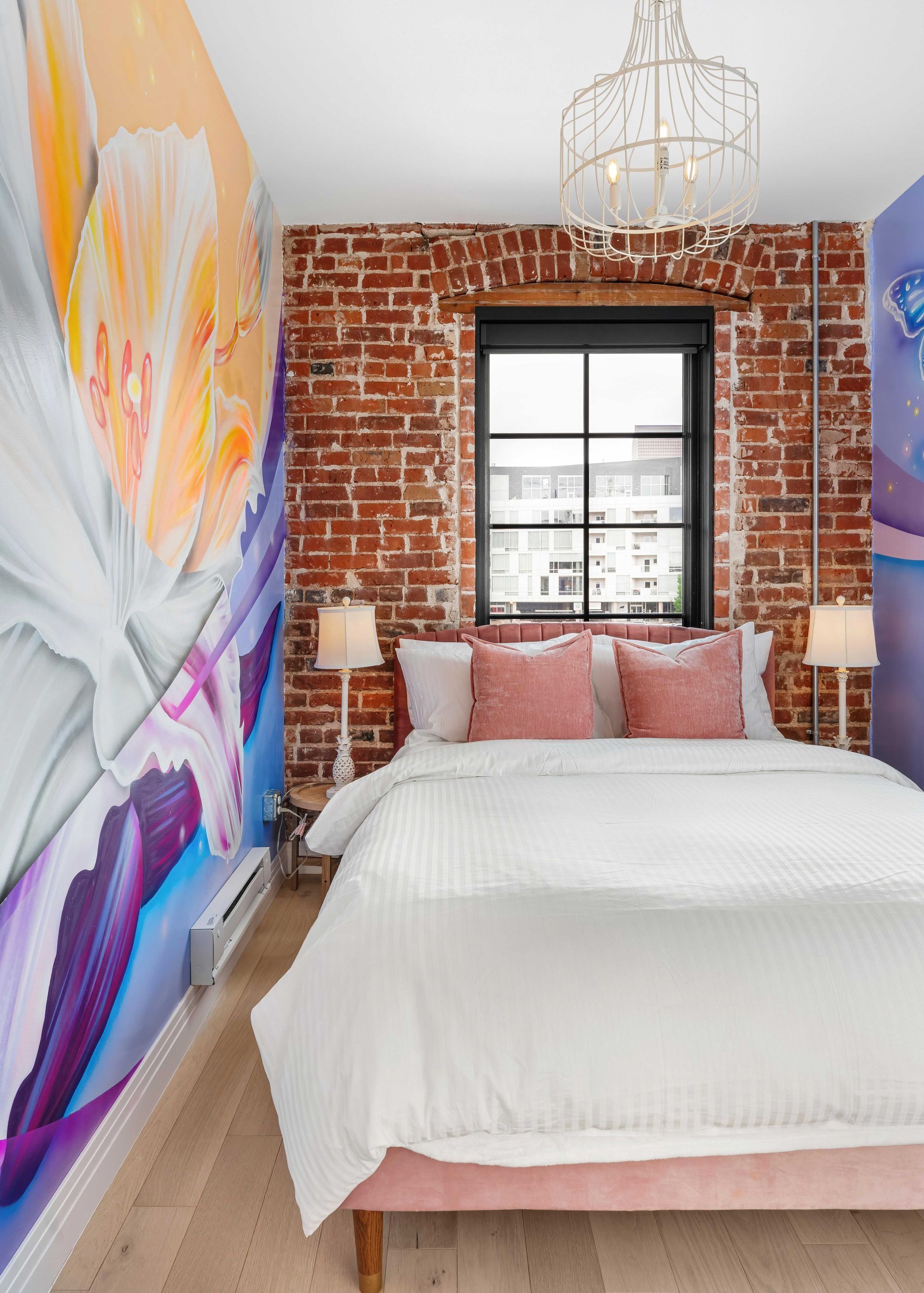 Stylish bedroom with exposed brick wall, colorful mural, white bed, and window above pink pillows