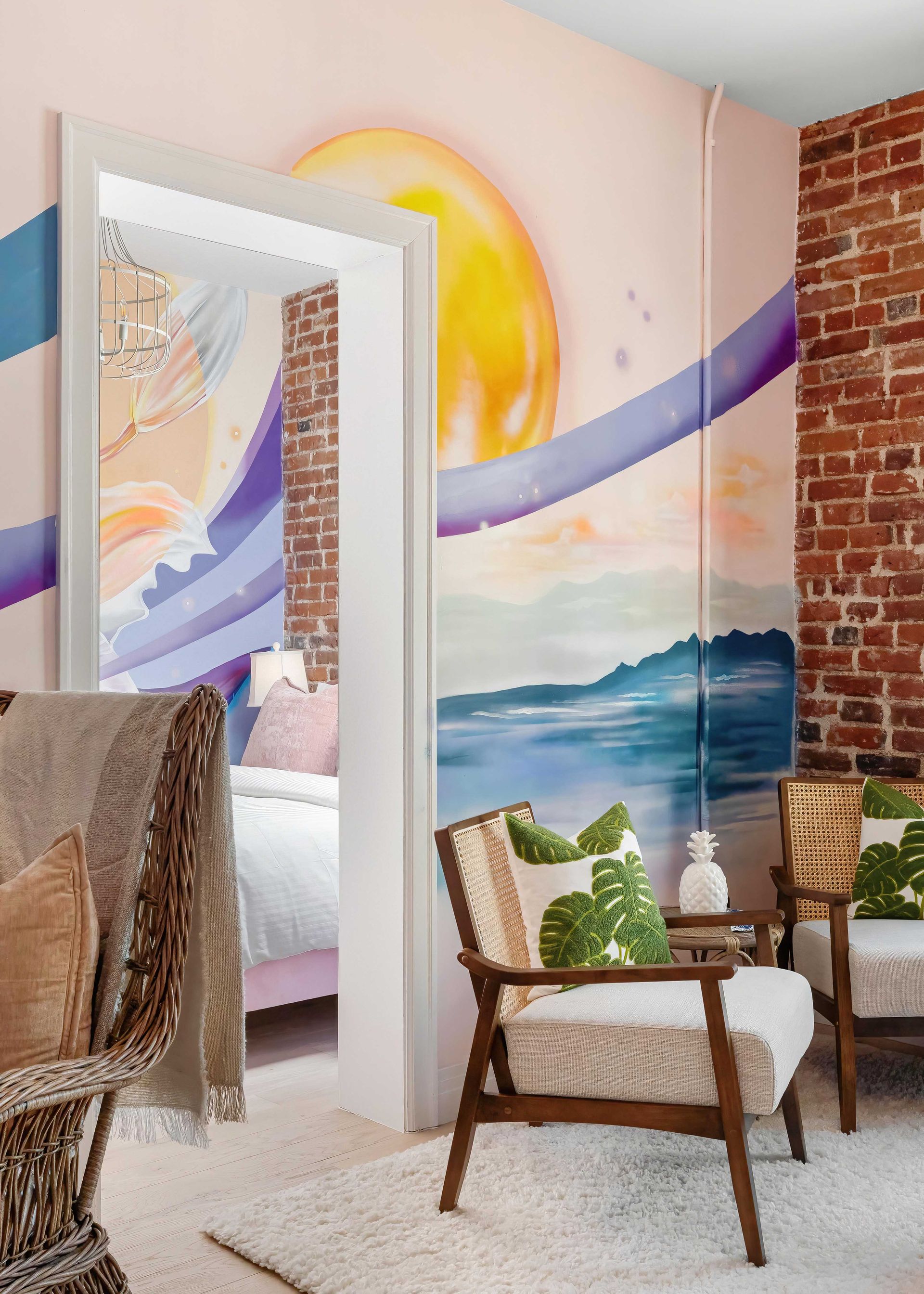 Bright coastal mural in a room with wicker chairs, a mirror, and brick wall detail