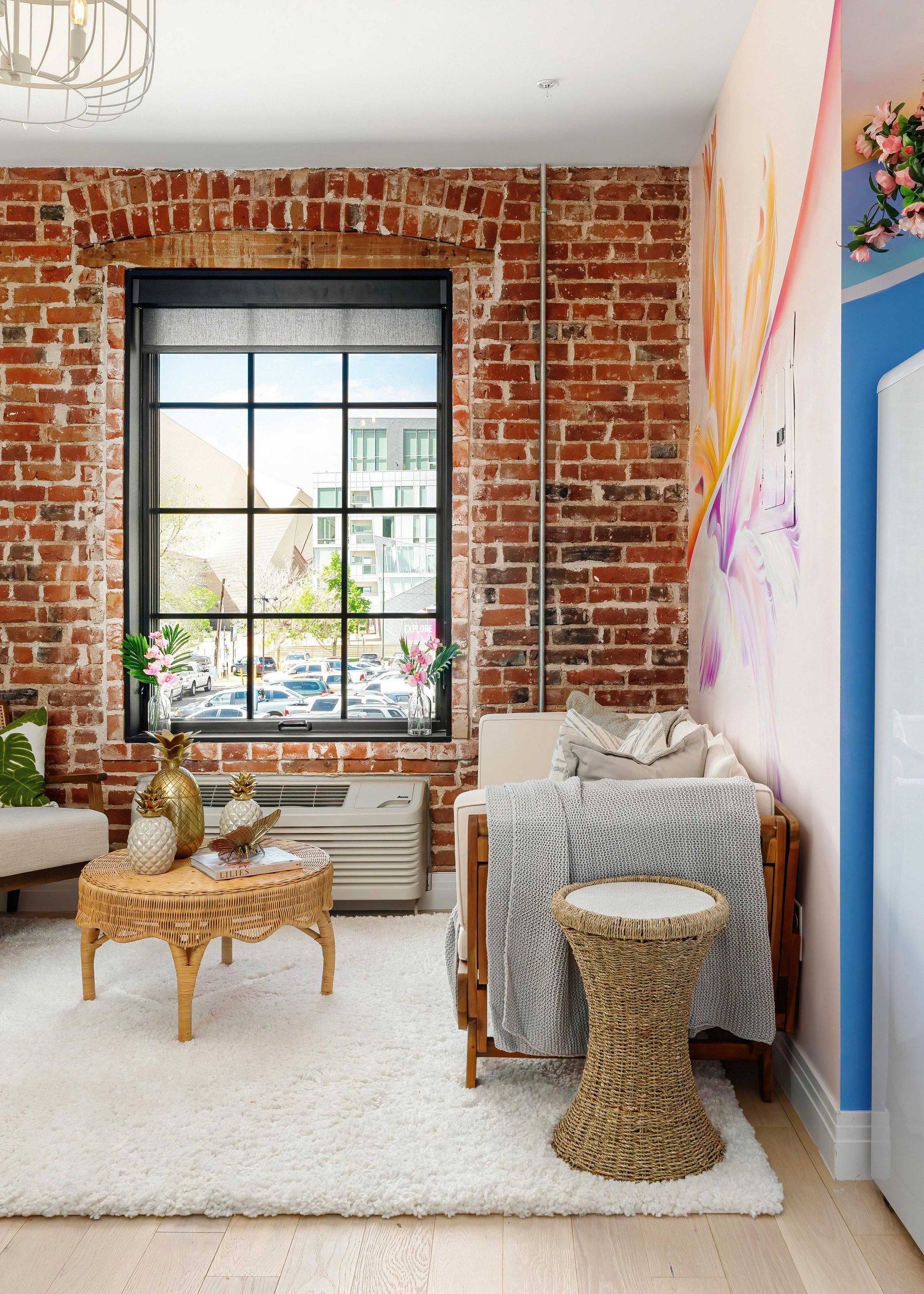 Cozy living room with exposed brick wall, large window, white rug, and patterned chairs and table