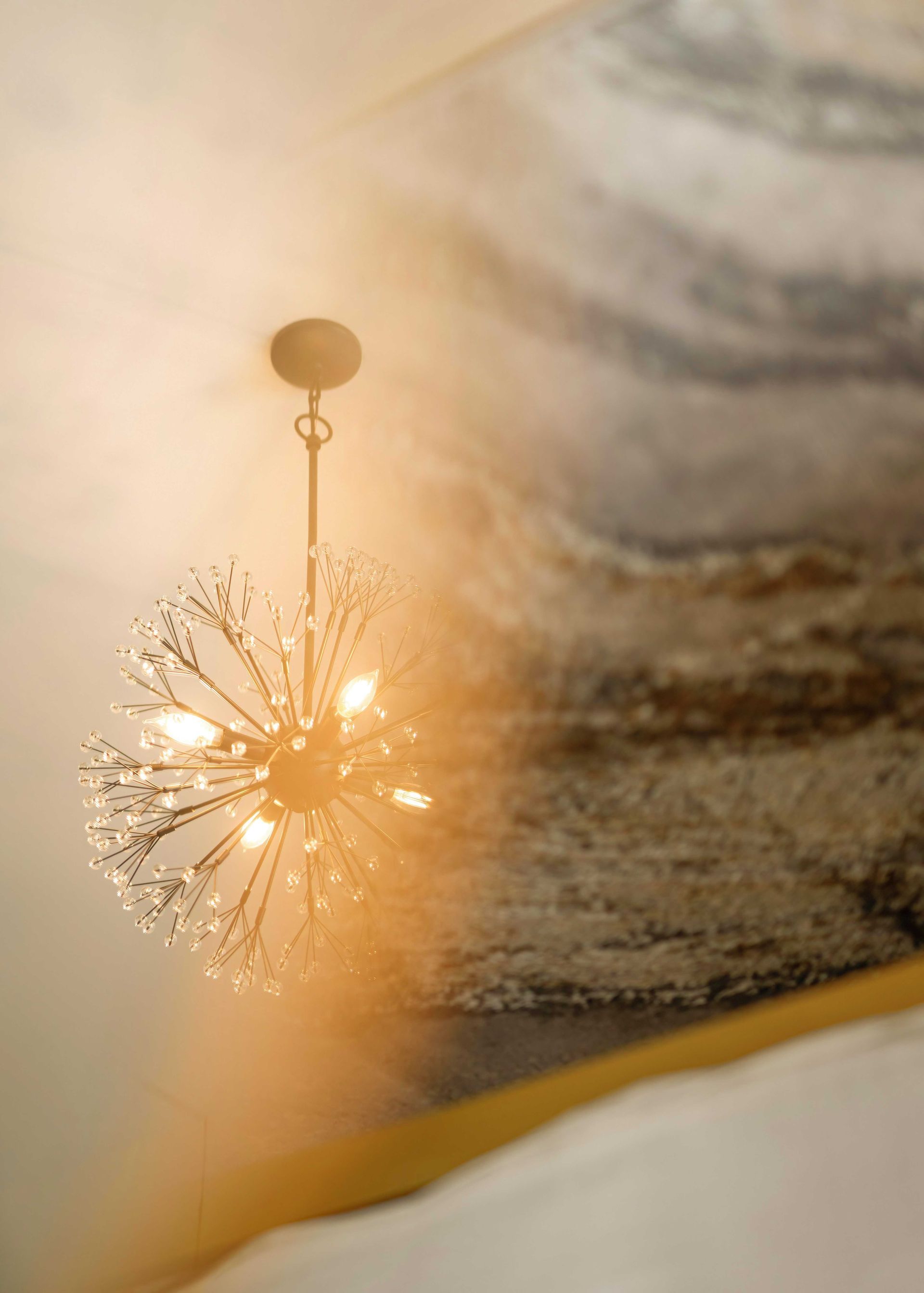 Glowing chandelier reflected in a mirror, with warm light and blurred decor in the background