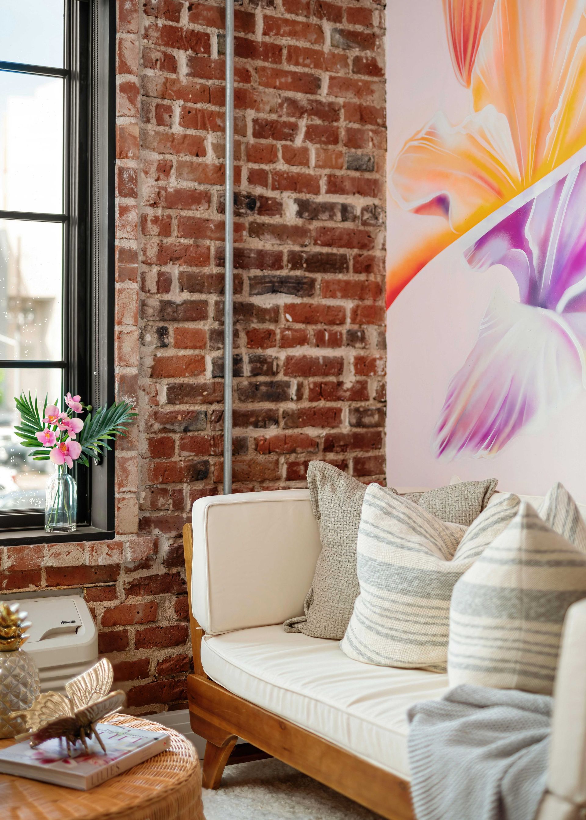 Cozy brick-walled reading nook with a cream loveseat, striped pillows, and a colorful floral wall print