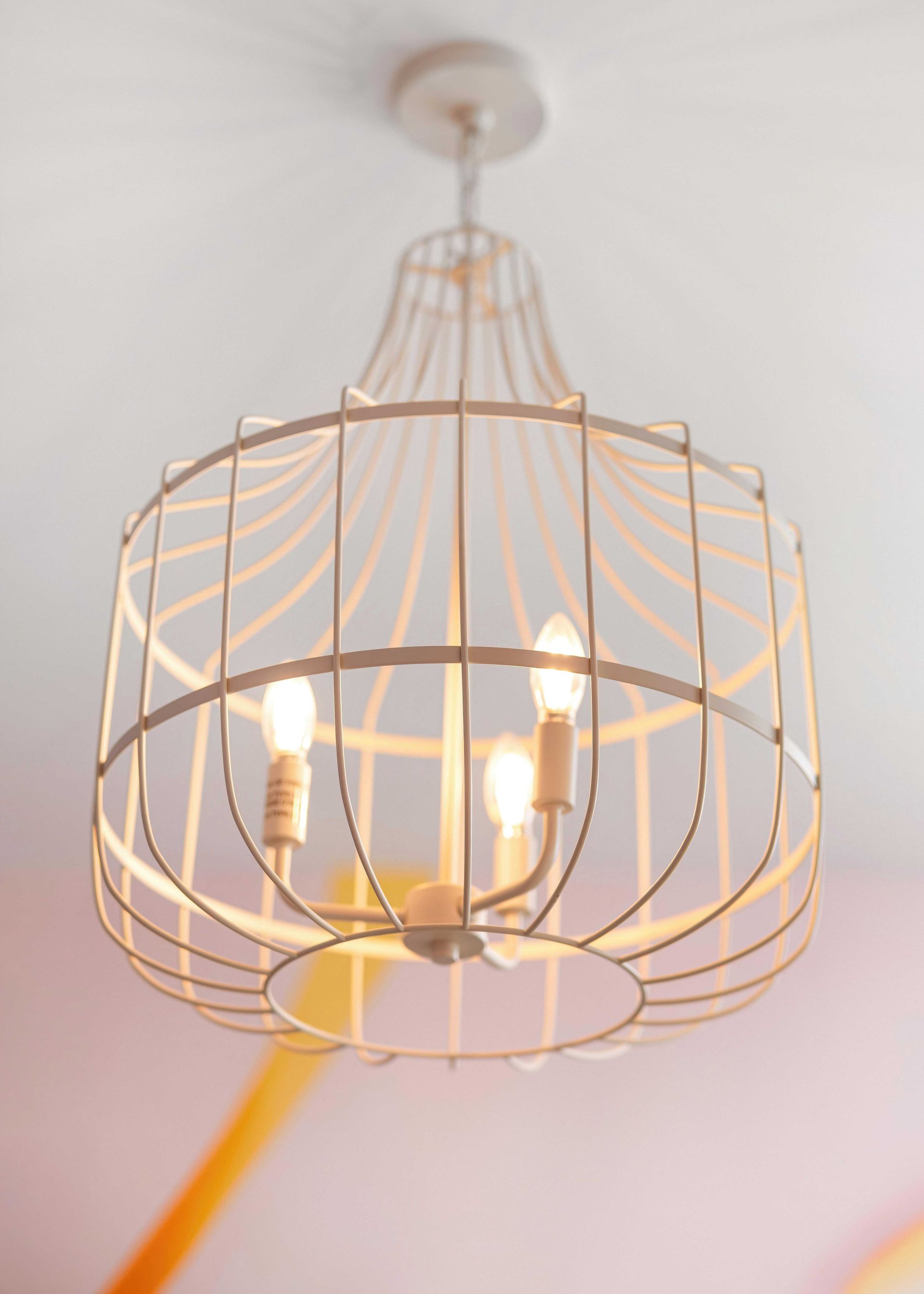 Gold wire cage pendant light with four bulbs hanging from a white ceiling