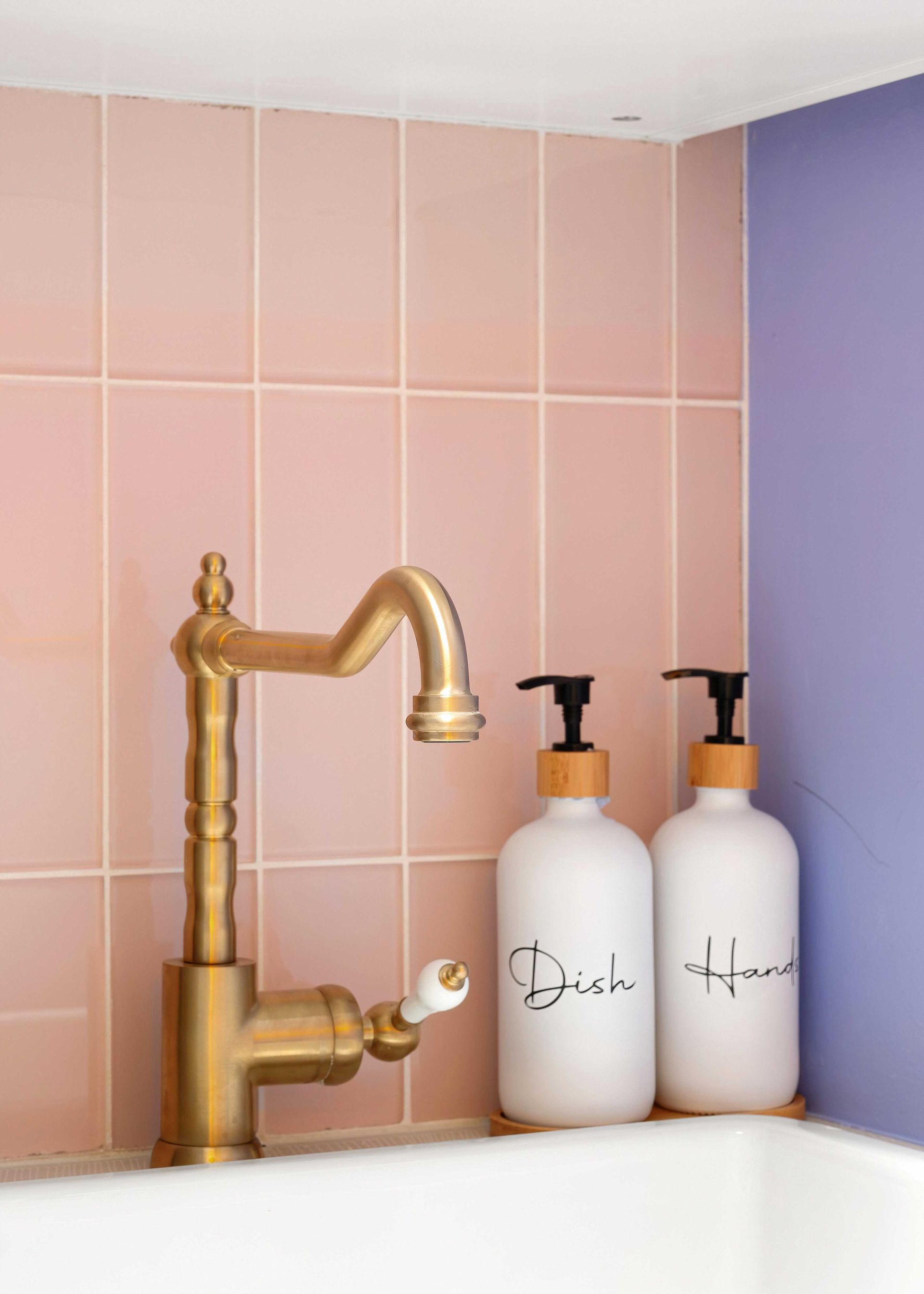 Brass faucet beside two white pump bottles on a pink-tiled bathroom sink