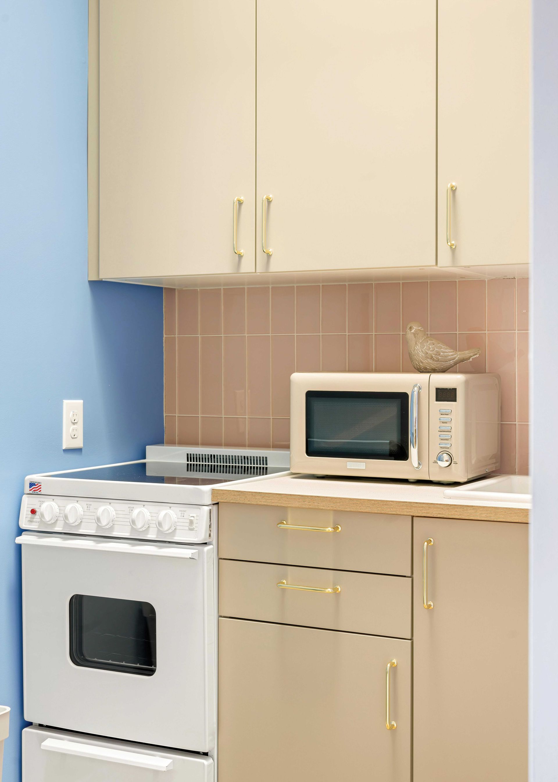 Small kitchen with beige cabinets, white stove, microwave, and blue wall accents.