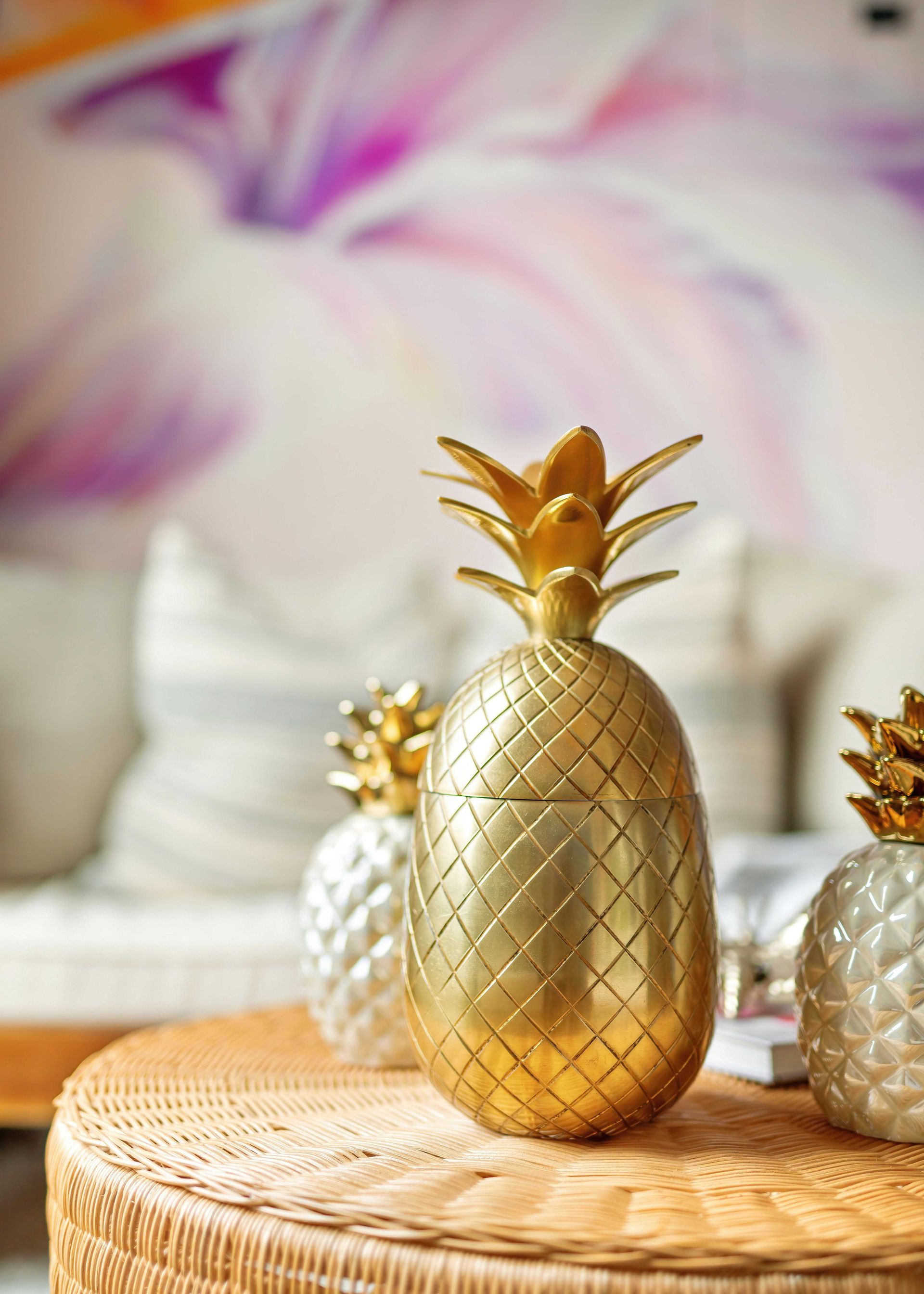Gold pineapple decor on a wicker tray with blurred pastel flowers in the background