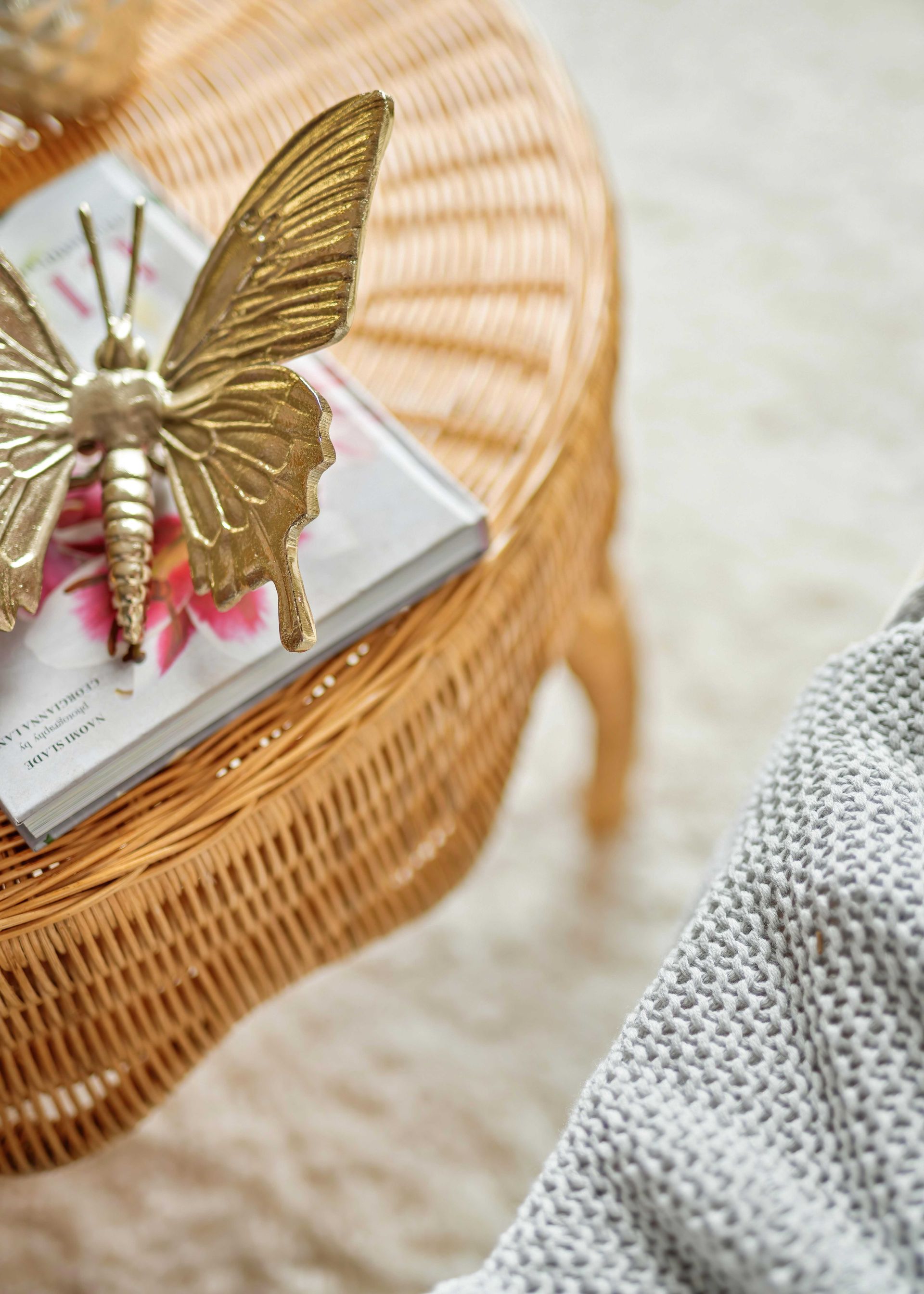 Gold butterfly ornament on a wicker table with a book and pink flowers.