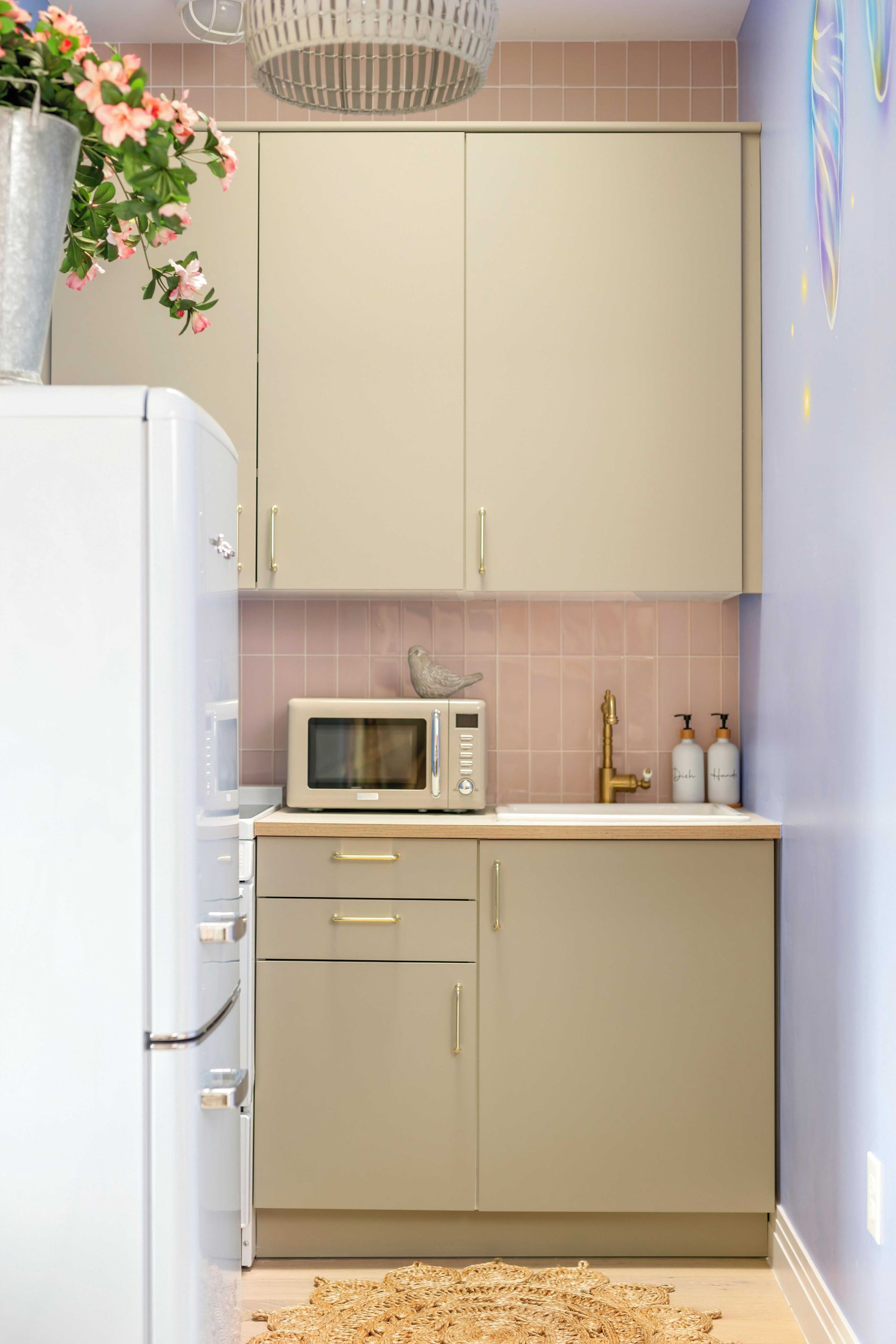 Compact kitchen with beige cabinets, white fridge, microwave, and pink tiled backsplash