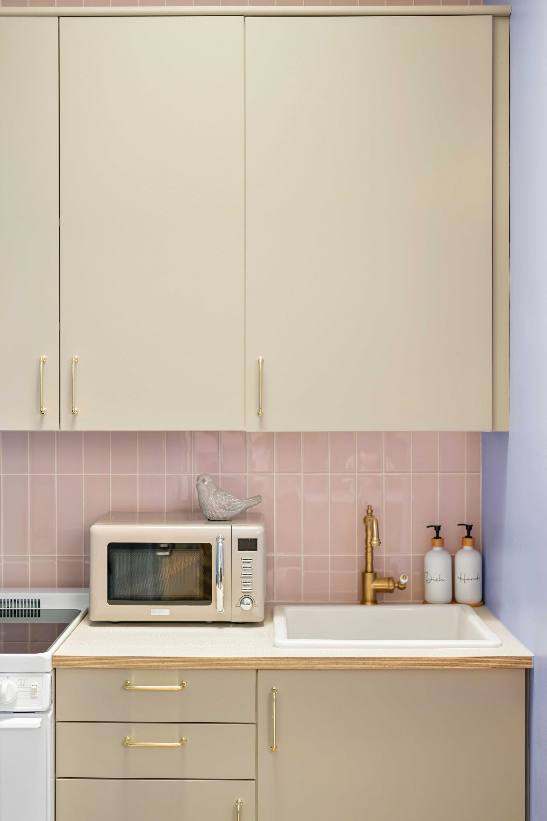 Modern kitchen with beige cabinets, pink backsplash, microwave, sink, and gold faucet and soap dispensers