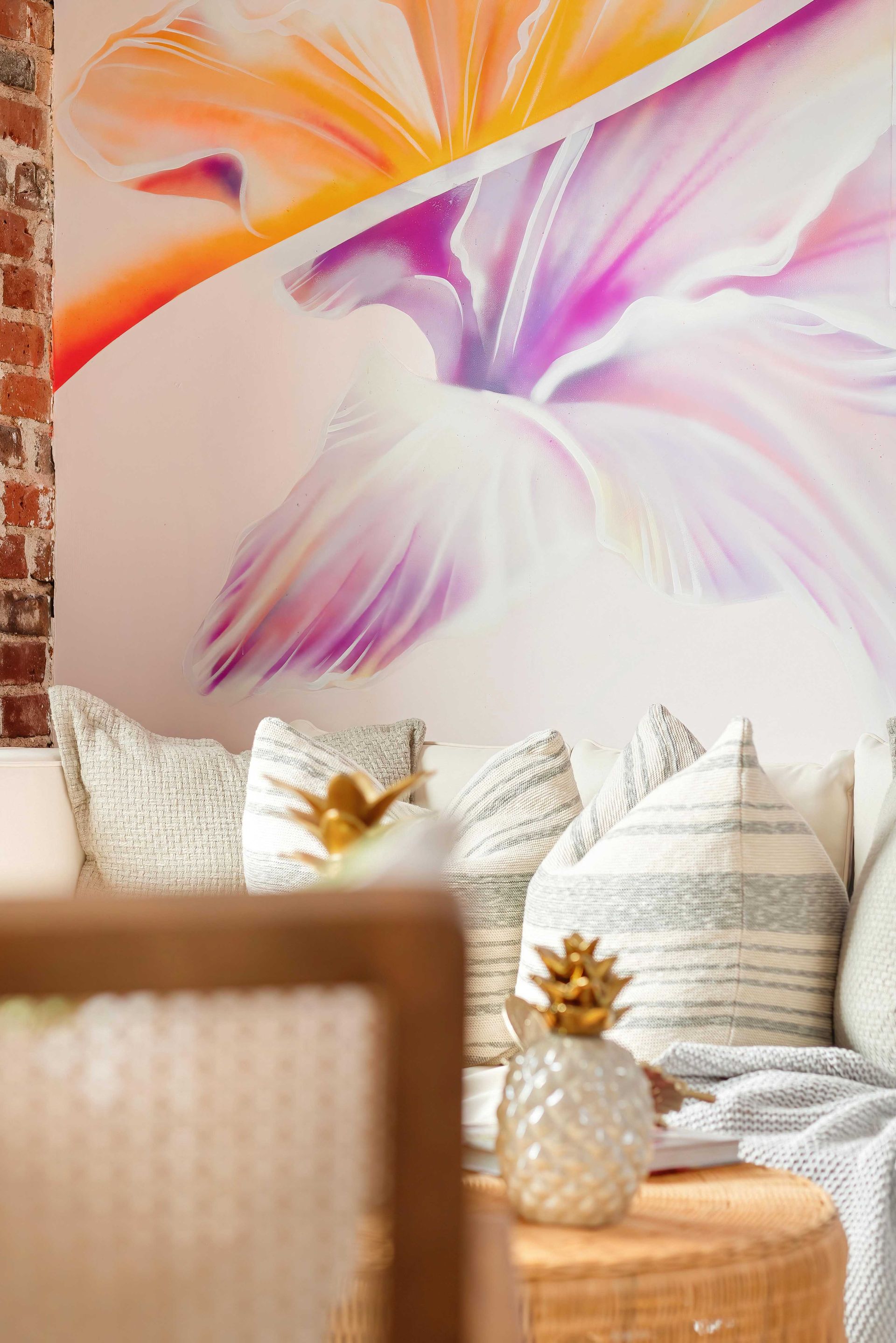 Colorful abstract floral wall art above a striped sofa with patterned pillows and a small pineapple decor piece