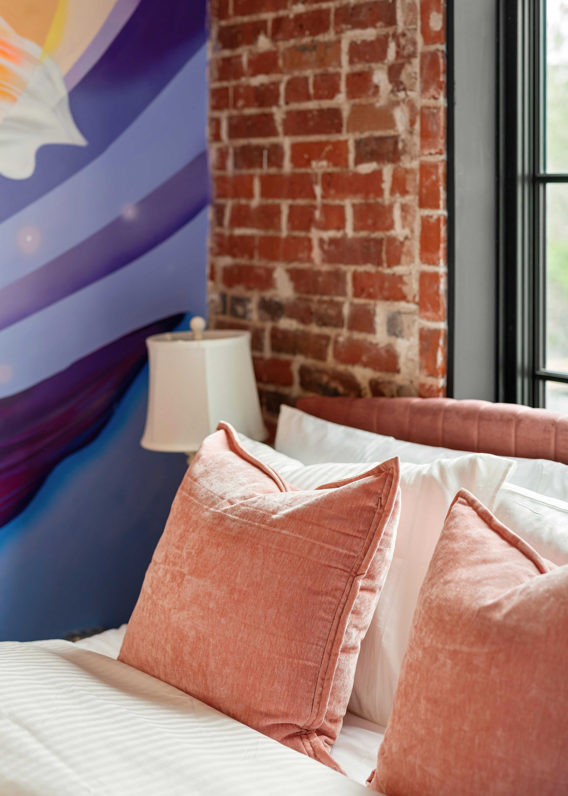 Cozy bed with pink pillows beside a brick wall and colorful mural in a room