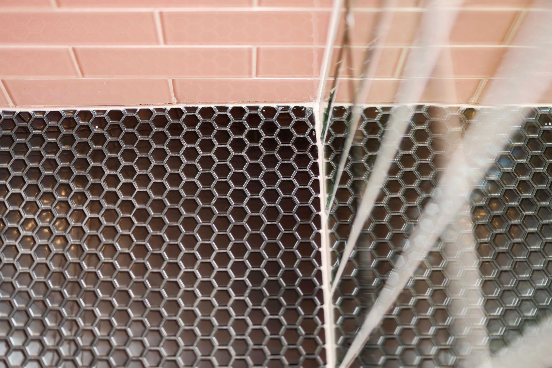 Black hexagonal tile floor beside pink wall and white metal bars, viewed at an angle