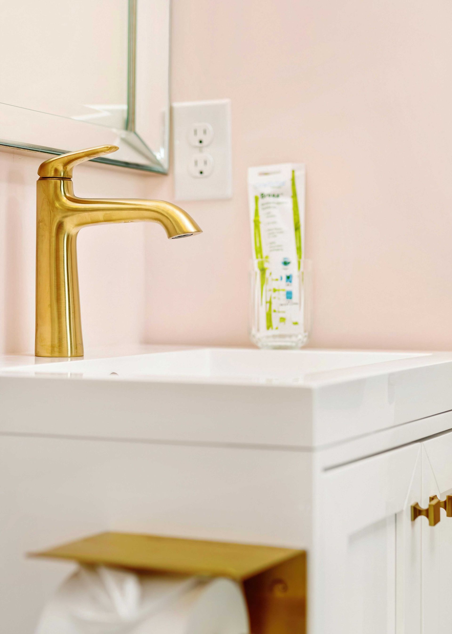 White bathroom vanity with gold faucet, mirror, outlet, and toothpaste tube on the counter