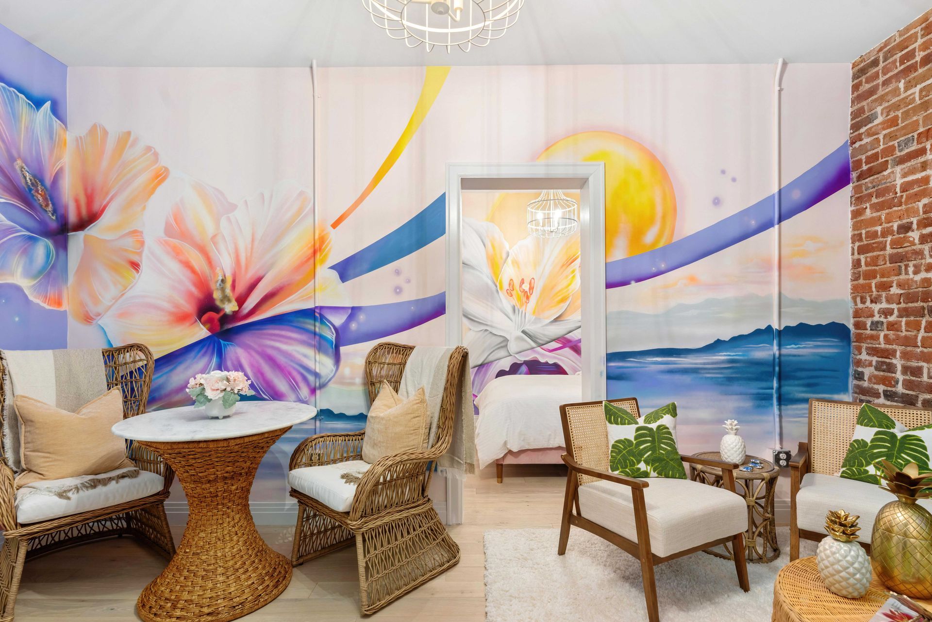 Bright mural-filled lounge with wicker chairs, a round table, and a doorway opening to a beach view.