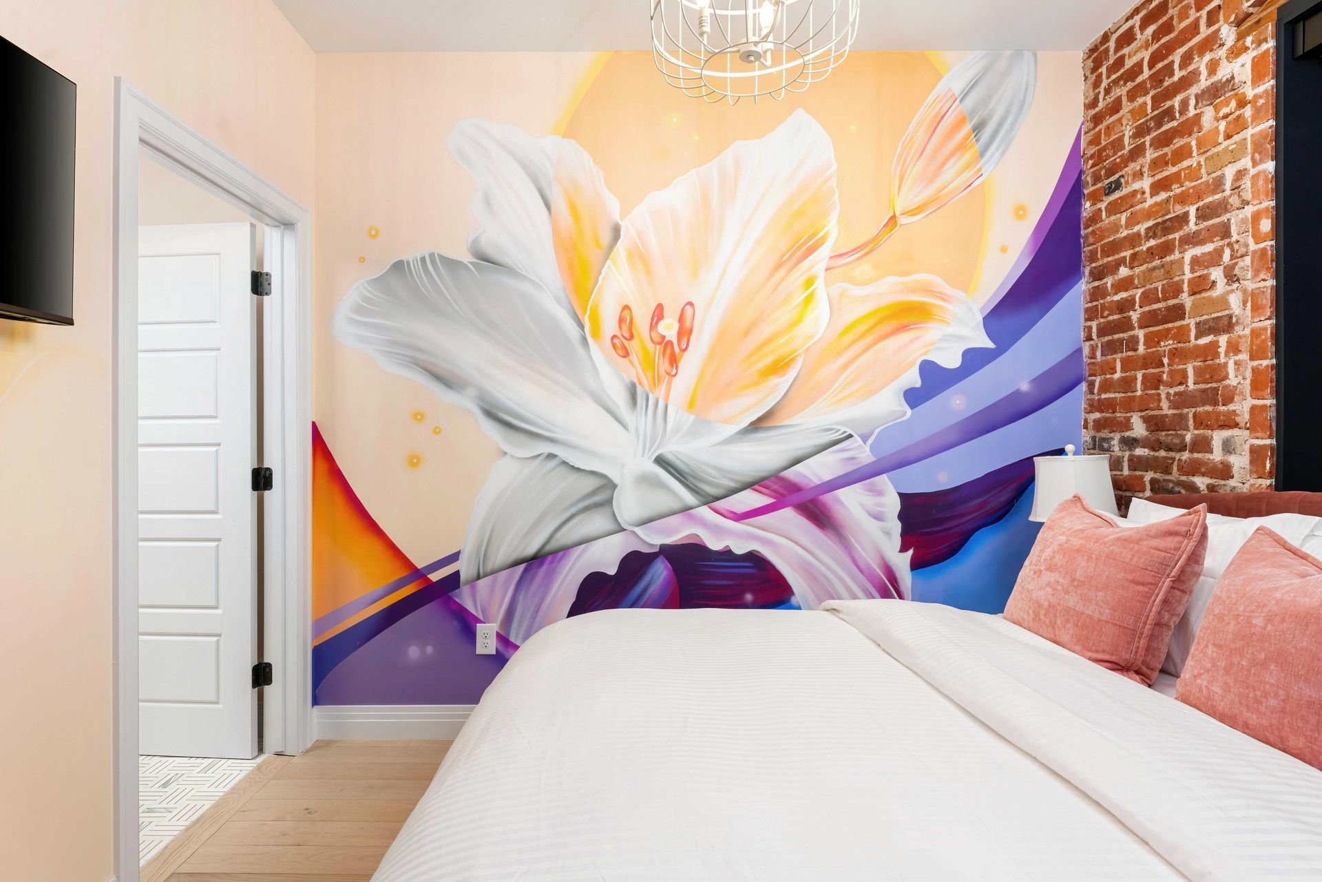 Bedroom with large white flower mural, purple accents, brick wall, and white bed with pink pillows