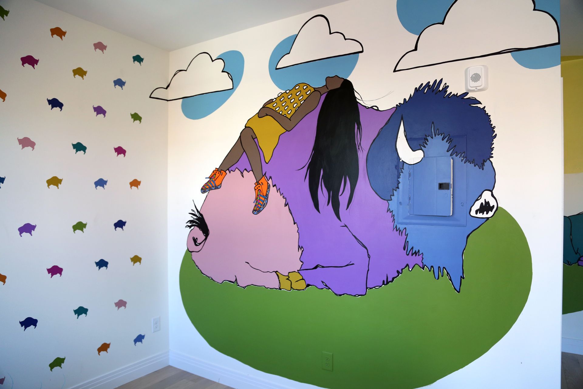 Colorful mural of three cartoon horses on a green hill with clouds and stars on the walls
