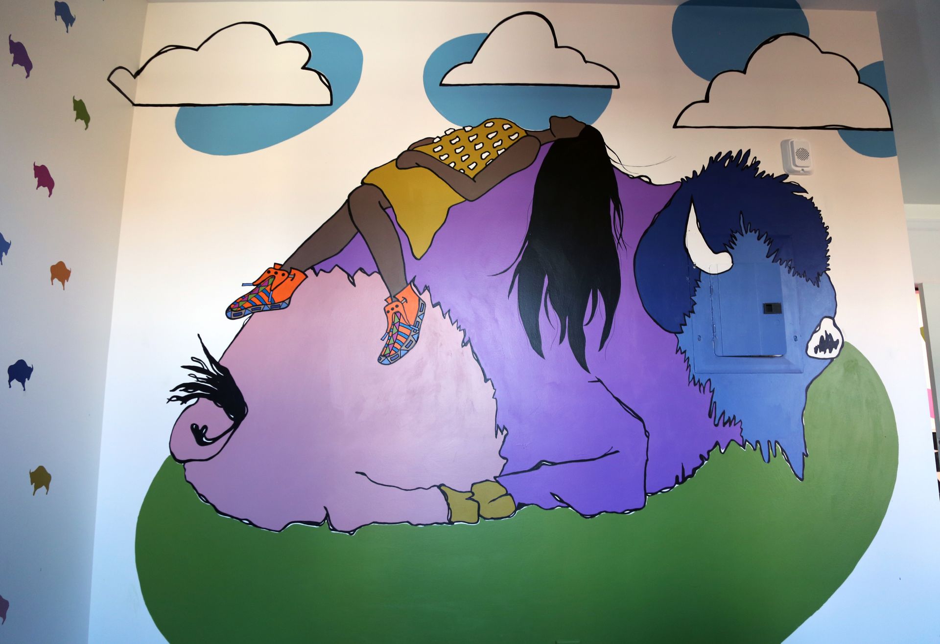 Mural of a purple, blue, and green creature lying under clouds in a whimsical landscape