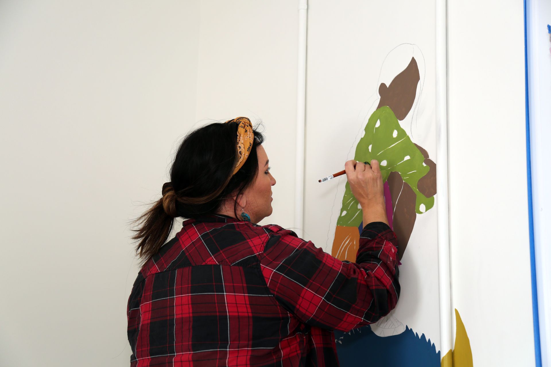 Person painting a colorful mural on a white wall indoors