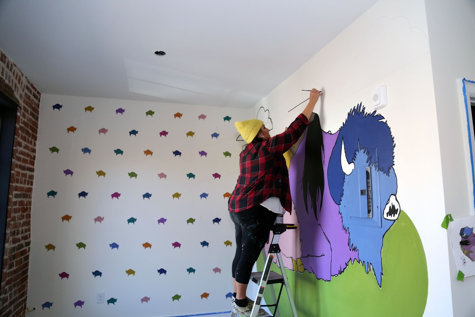 Person on a ladder painting a colorful mural on a wall in a room