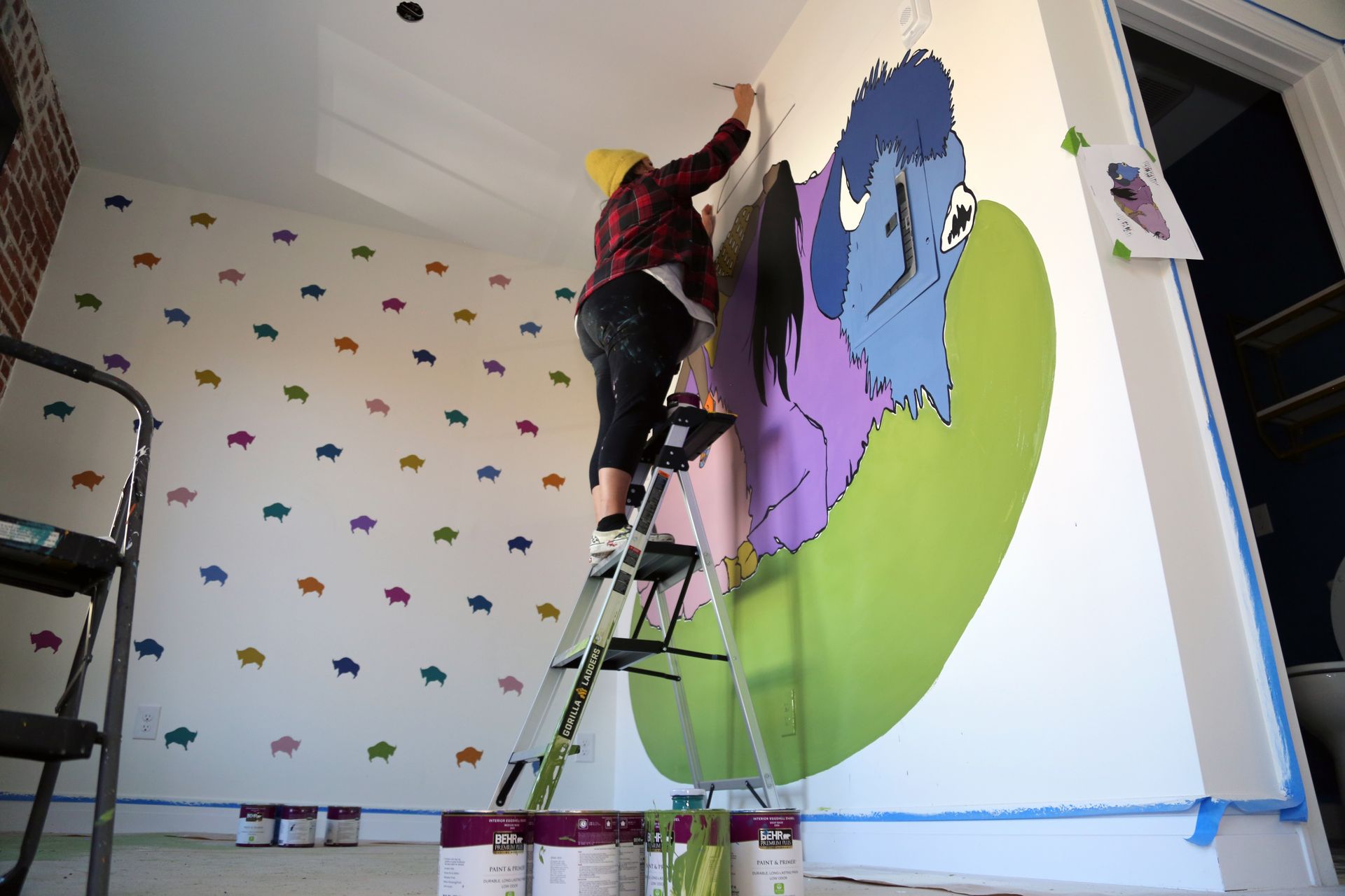 Person painting a colorful mural on a wall while standing on a ladder in a room
