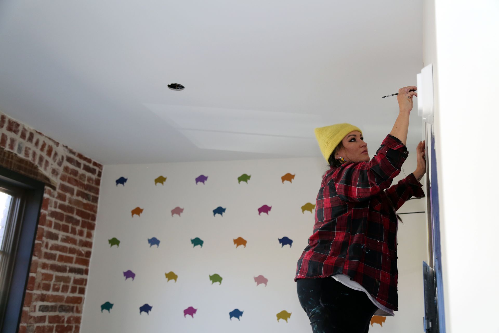 Person painting a wall in a room with colorful star decals and exposed brick accents