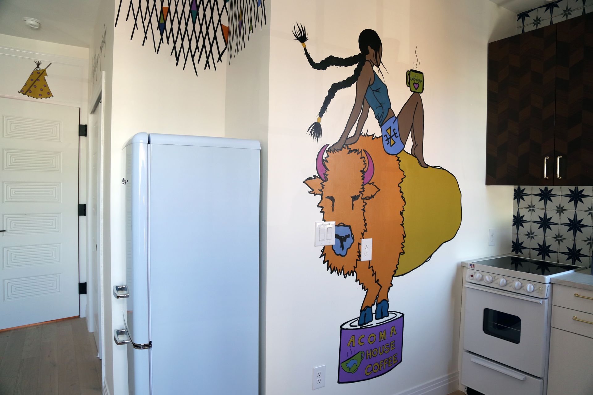 Kitchen with a colorful wall mural of a woman riding a lion beside a fridge and stove.