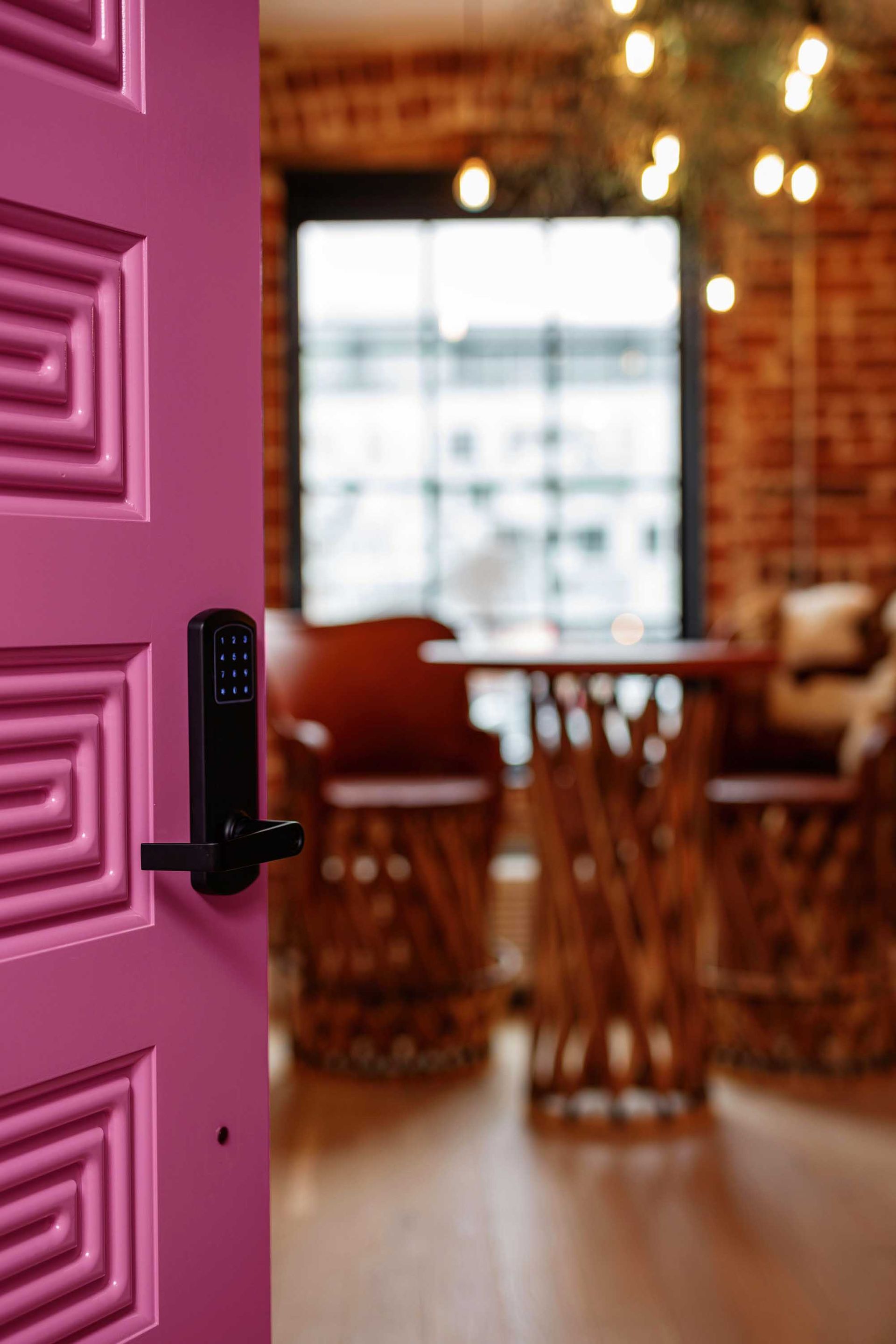 Open pink door leading into a cozy café with wooden tables and warm hanging lights
