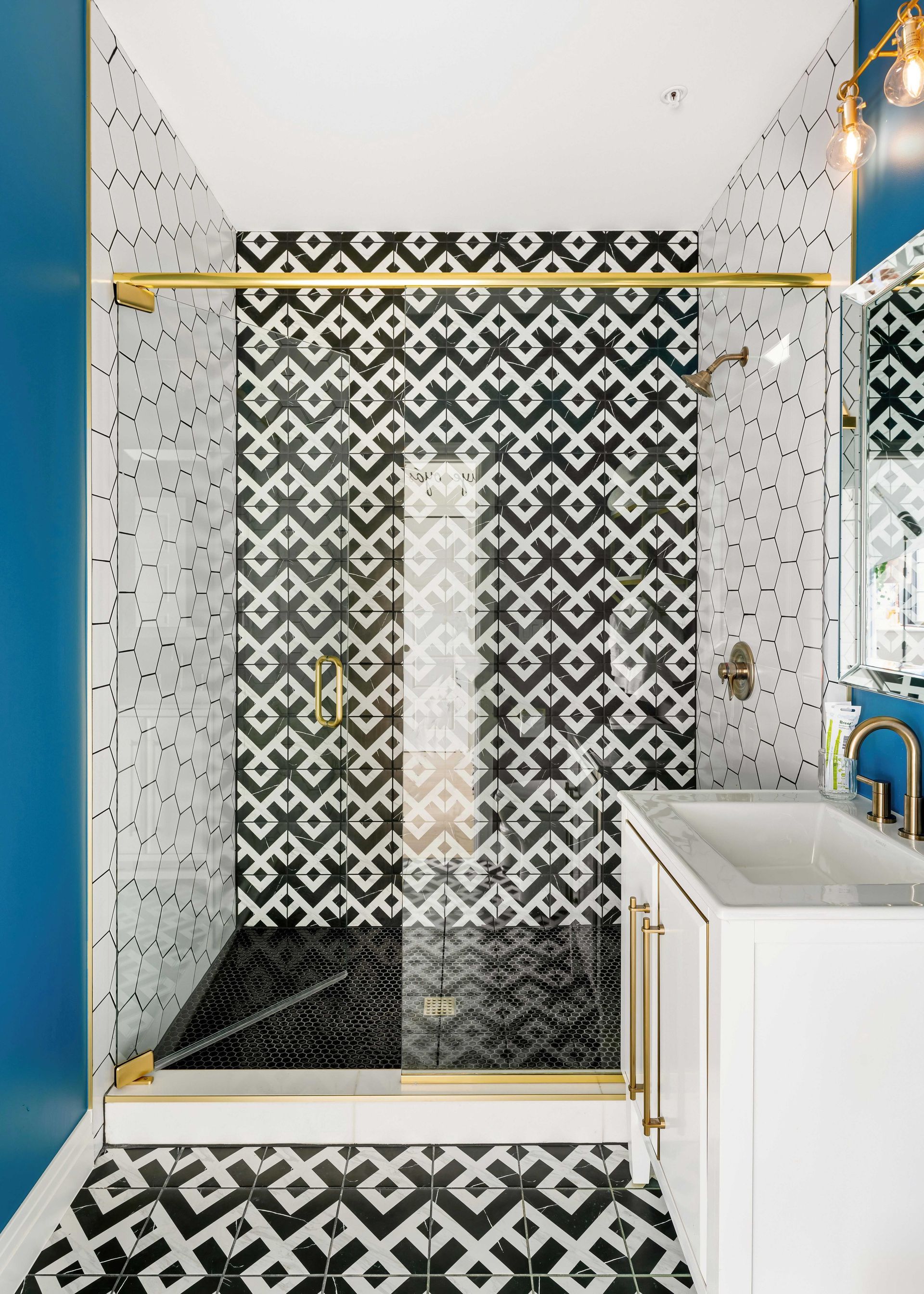 Modern shower stall with black-and-white patterned tile and a glass door beside a white vanity.