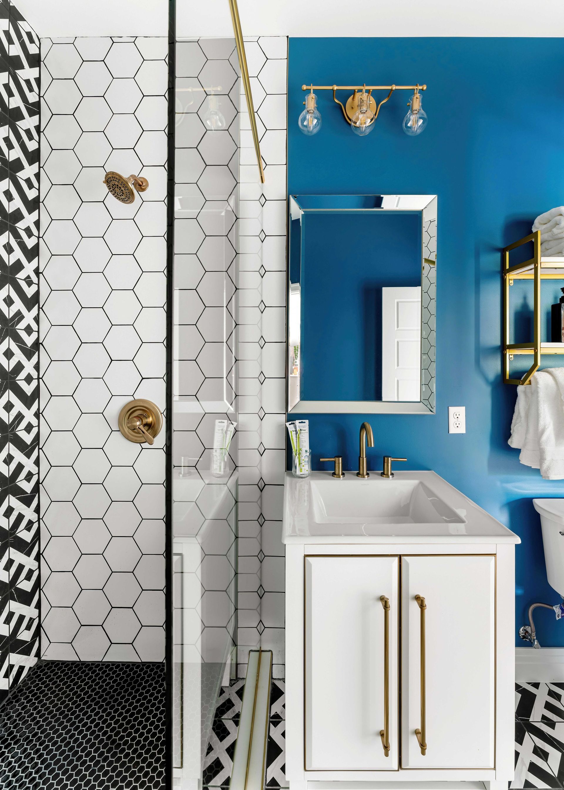 Blue bathroom with white vanity, mirror, and black-and-white hex tile shower.