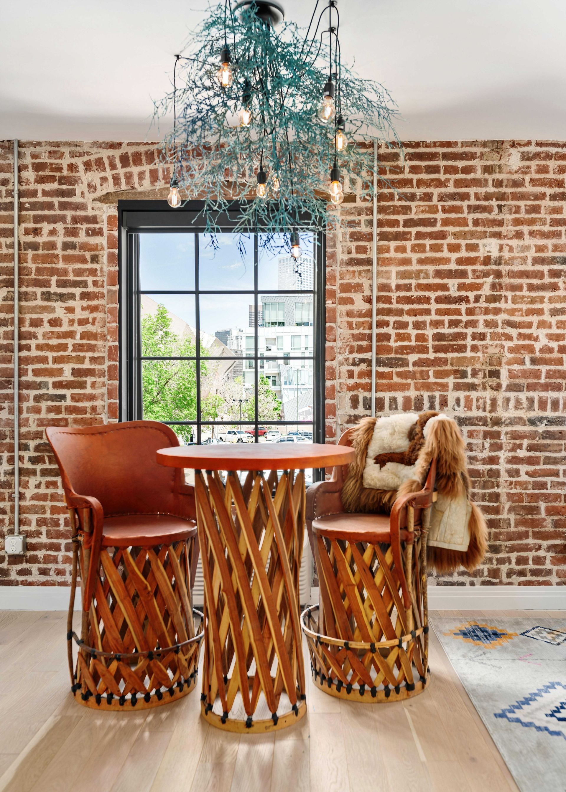 Rustic dining nook with brick walls, woven chairs, a round table, and a hanging blue chandelier by a large window