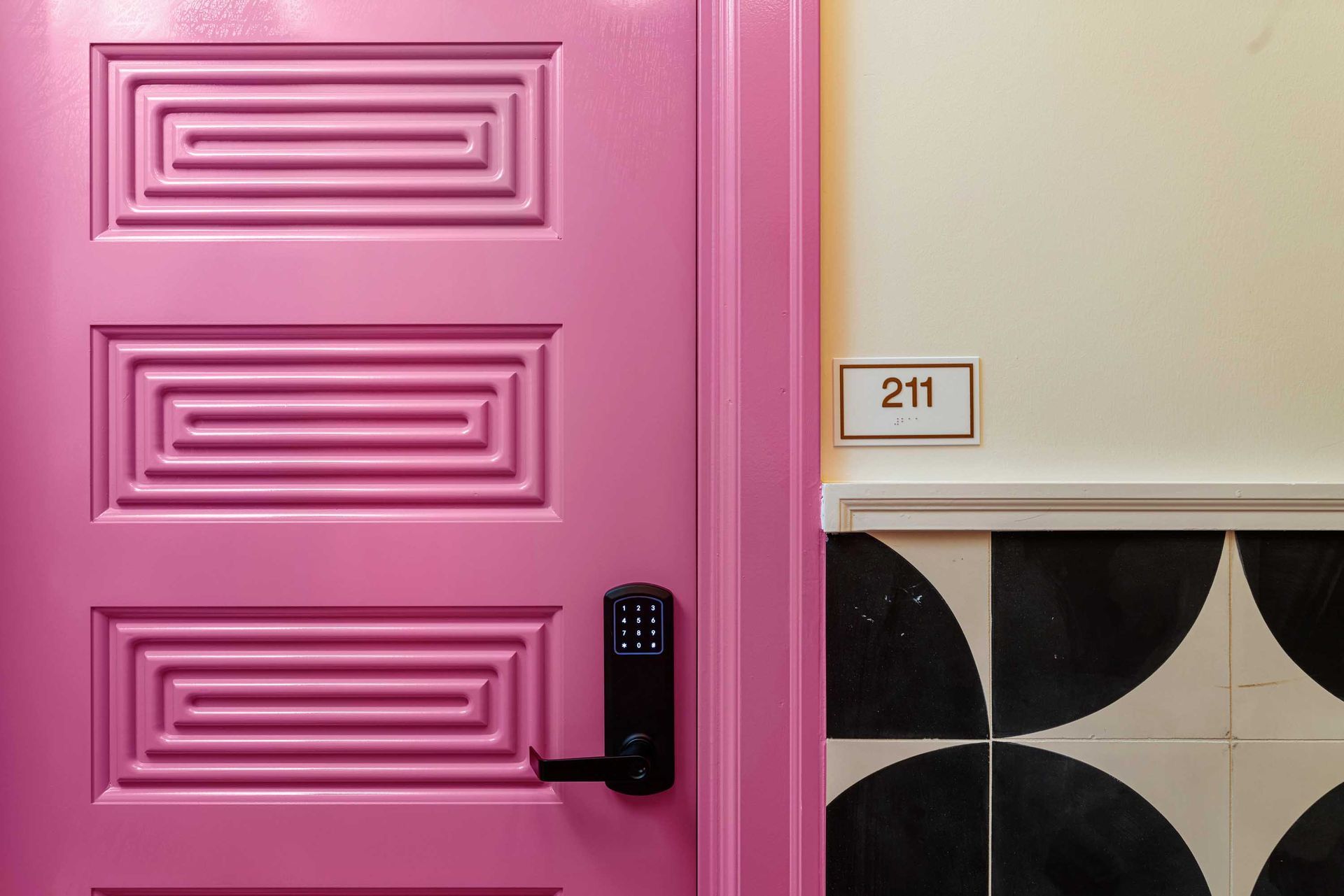 Pink door with black handle beside room number 211 and black-and-white tiled wall