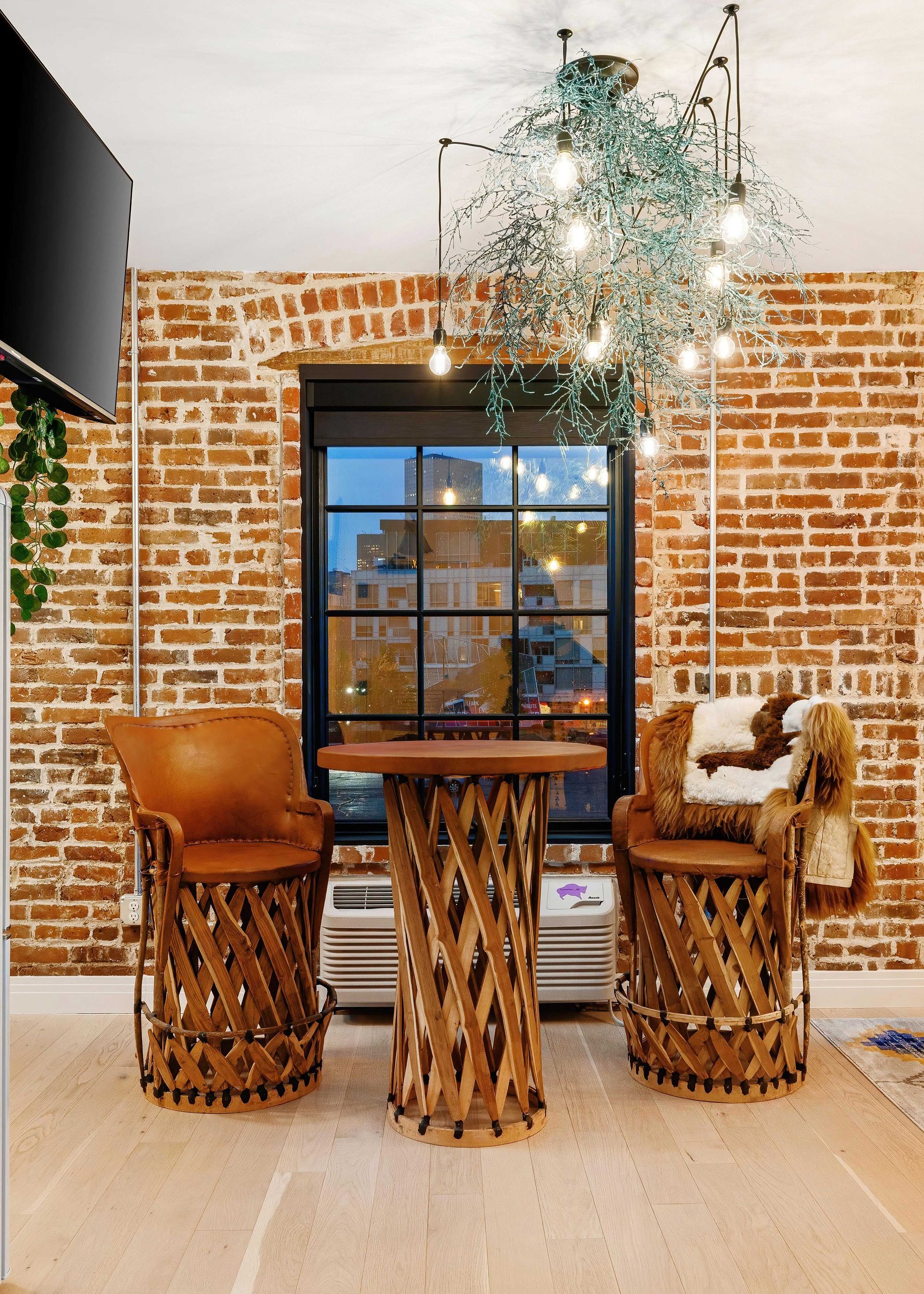Cozy dining nook with brick wall, wicker chairs, rustic table, and hanging chandelier.