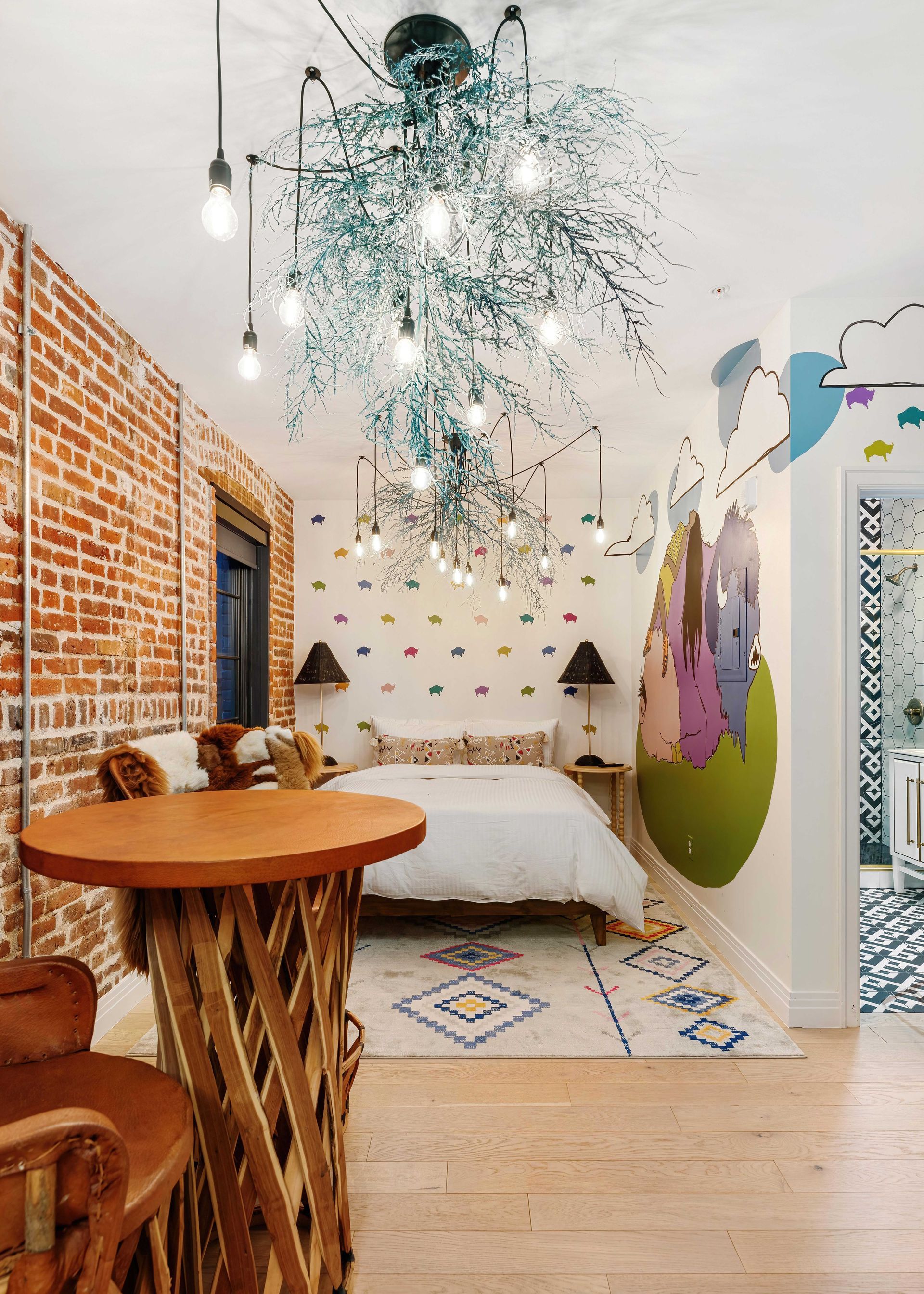 Cozy bedroom with brick wall, white bed, round table, and a large crystal chandelier overhead