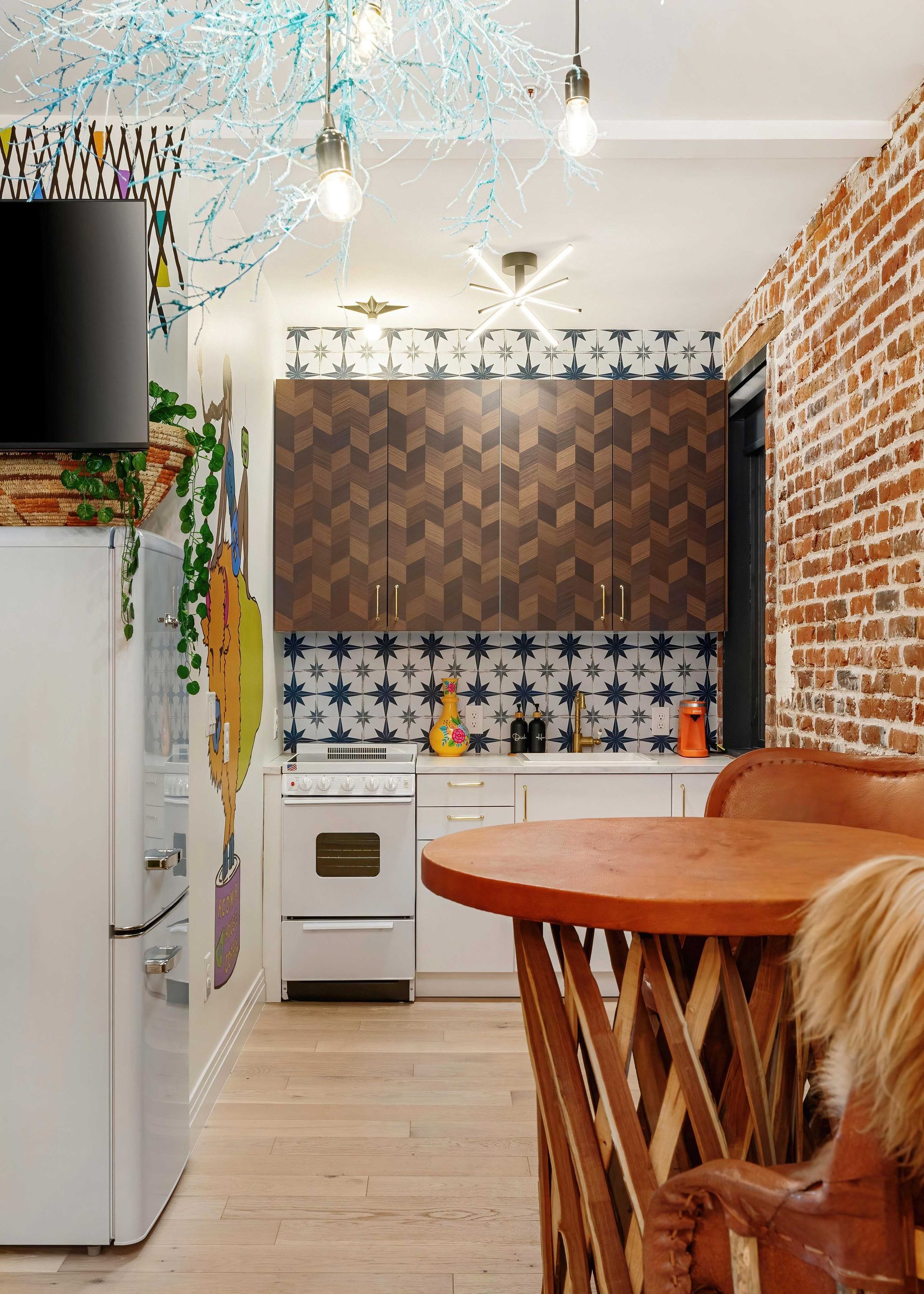 Bright compact kitchen with brick wall, white appliances, patterned tile backsplash, and round wooden table