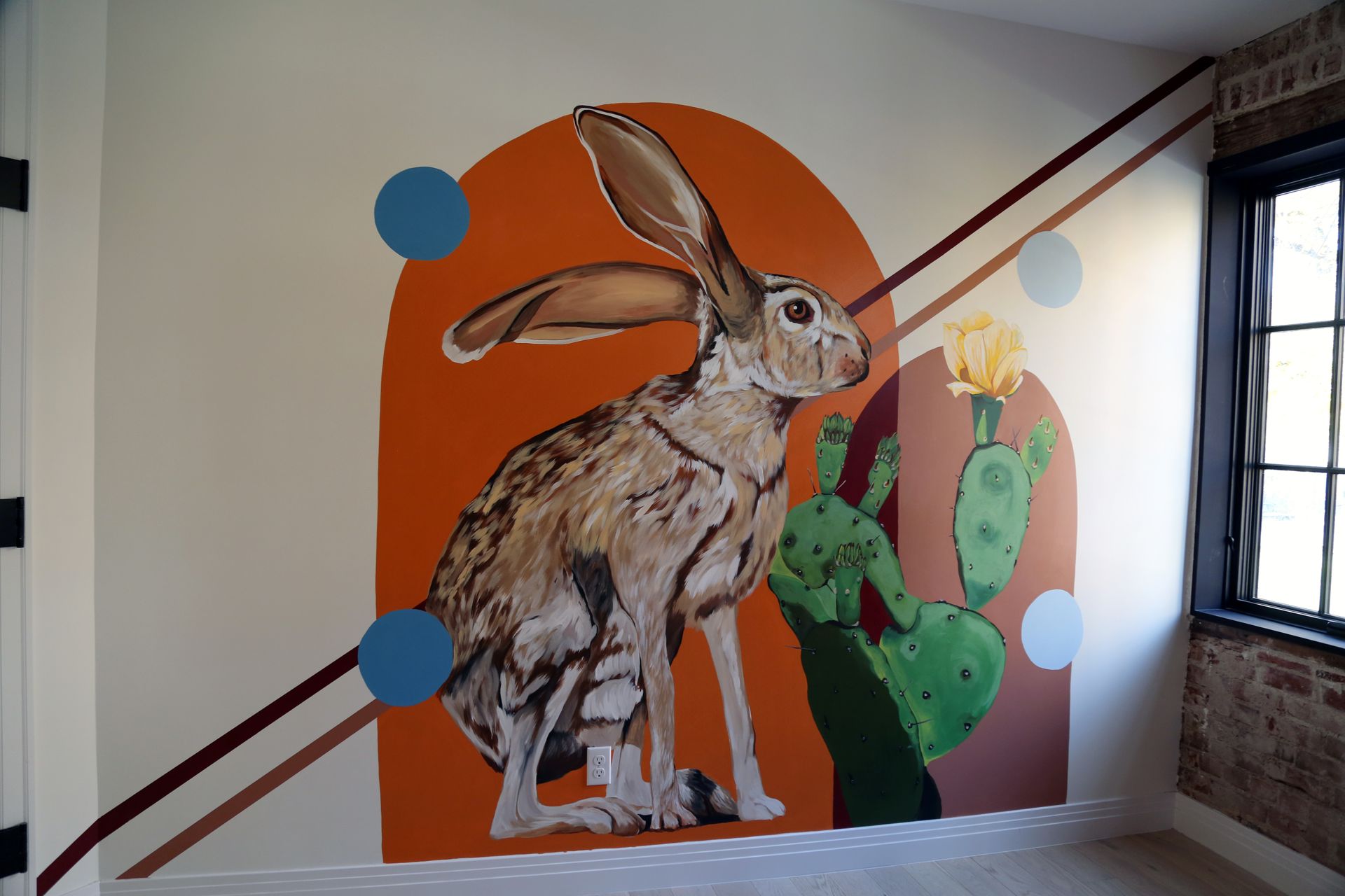 Mural of a large rabbit and cactus on a stairwell wall with orange and blue circles.