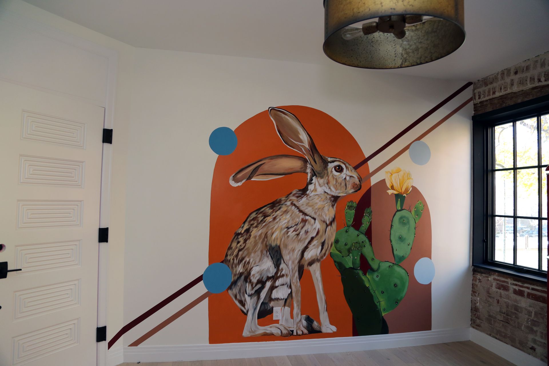 Rabbit mural on an orange wall in a room, with green cacti and blue dots beside a window