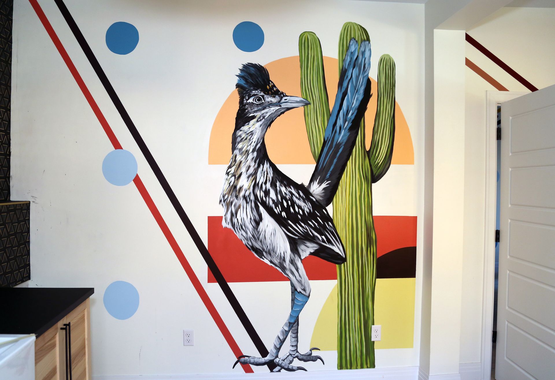 Mural of a bird beside a cactus with blue dots and diagonal stripes on a wall