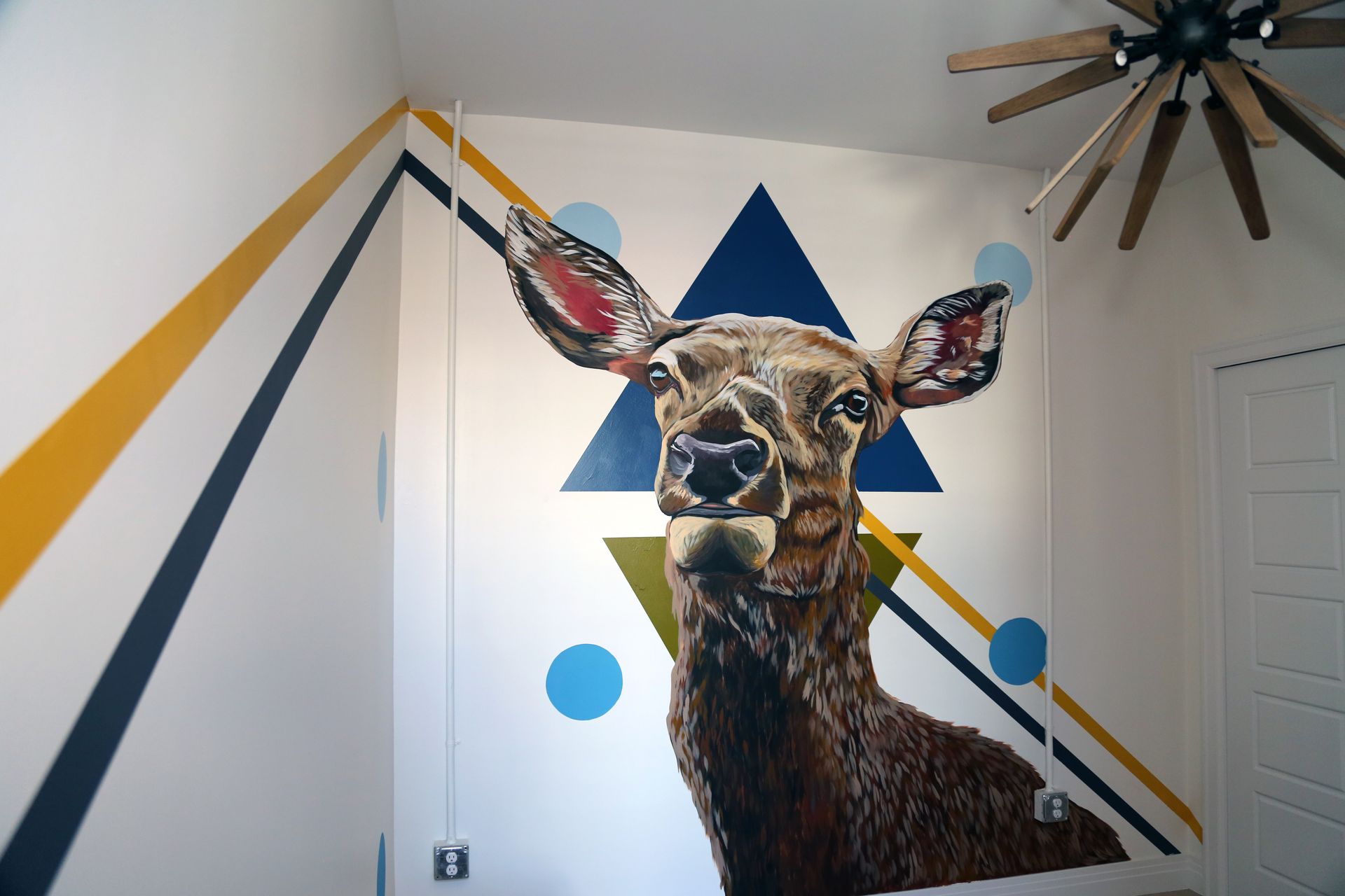 Wall mural of a deer with geometric blue, yellow, and white accents in a room