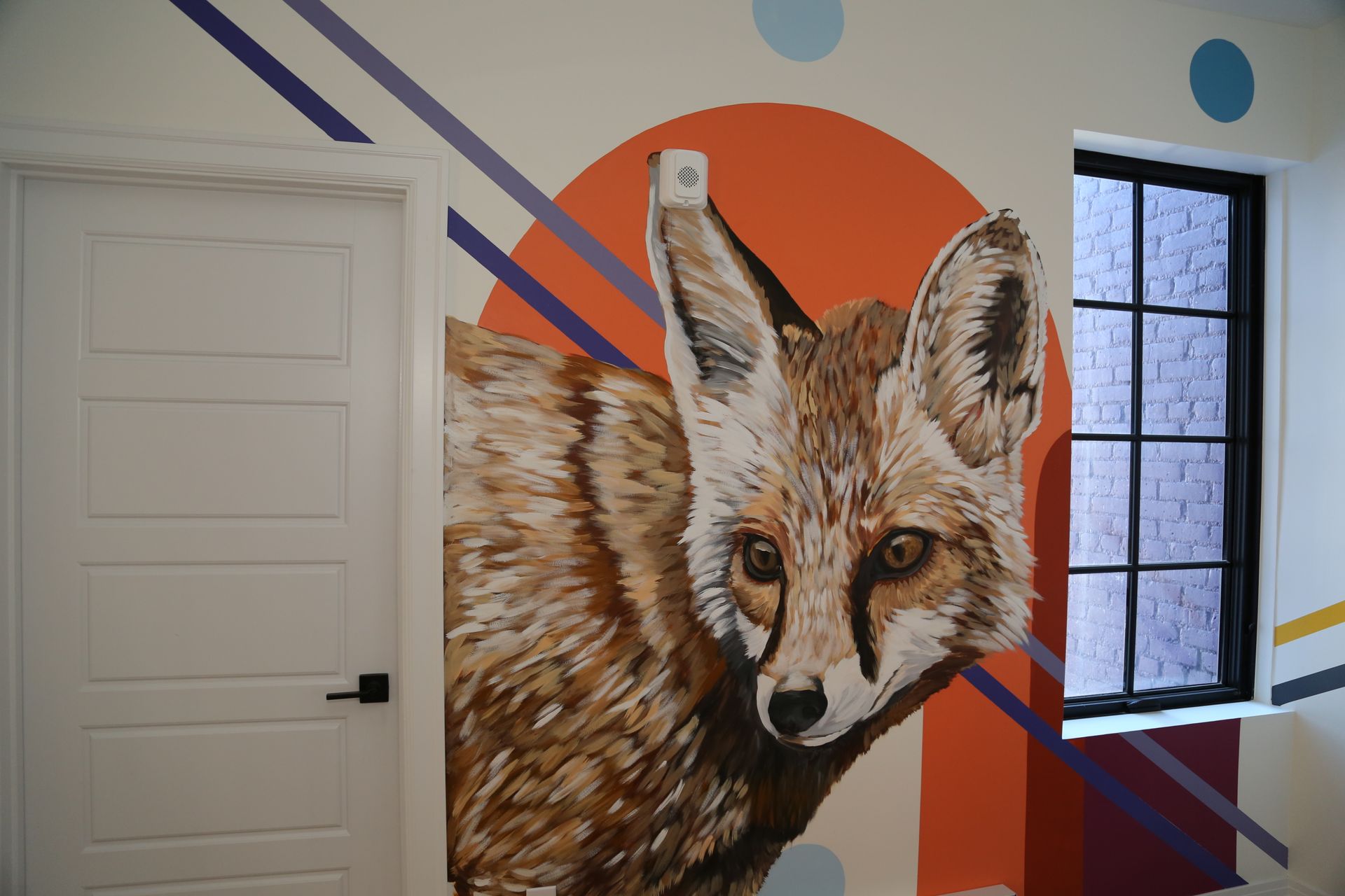 Mural of a fox on a white wall beside a door and window, with orange and purple geometric accents