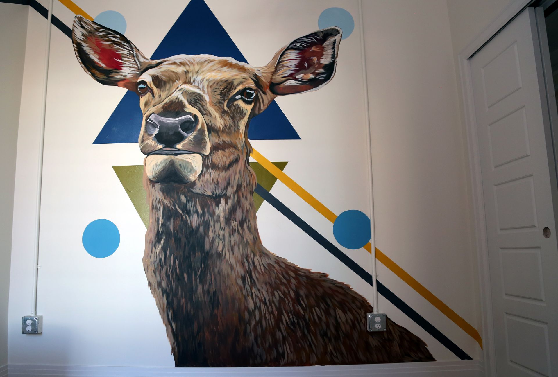 Large deer mural on a wall with blue circles and diagonal yellow, blue, and gray lines