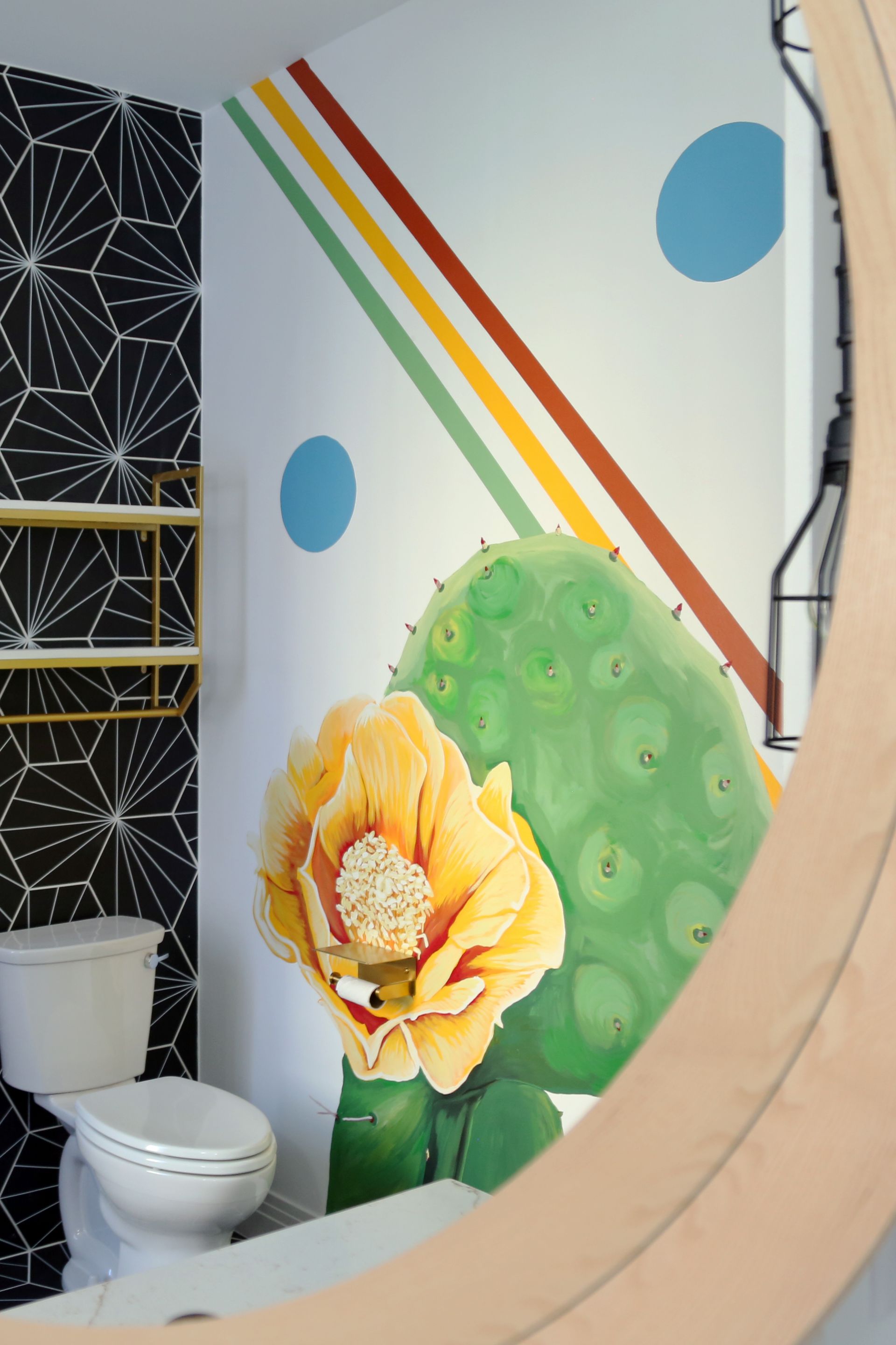 Colorful bathroom wall mural with flowers, cactus, blue dots, and rainbow stripes behind a toilet