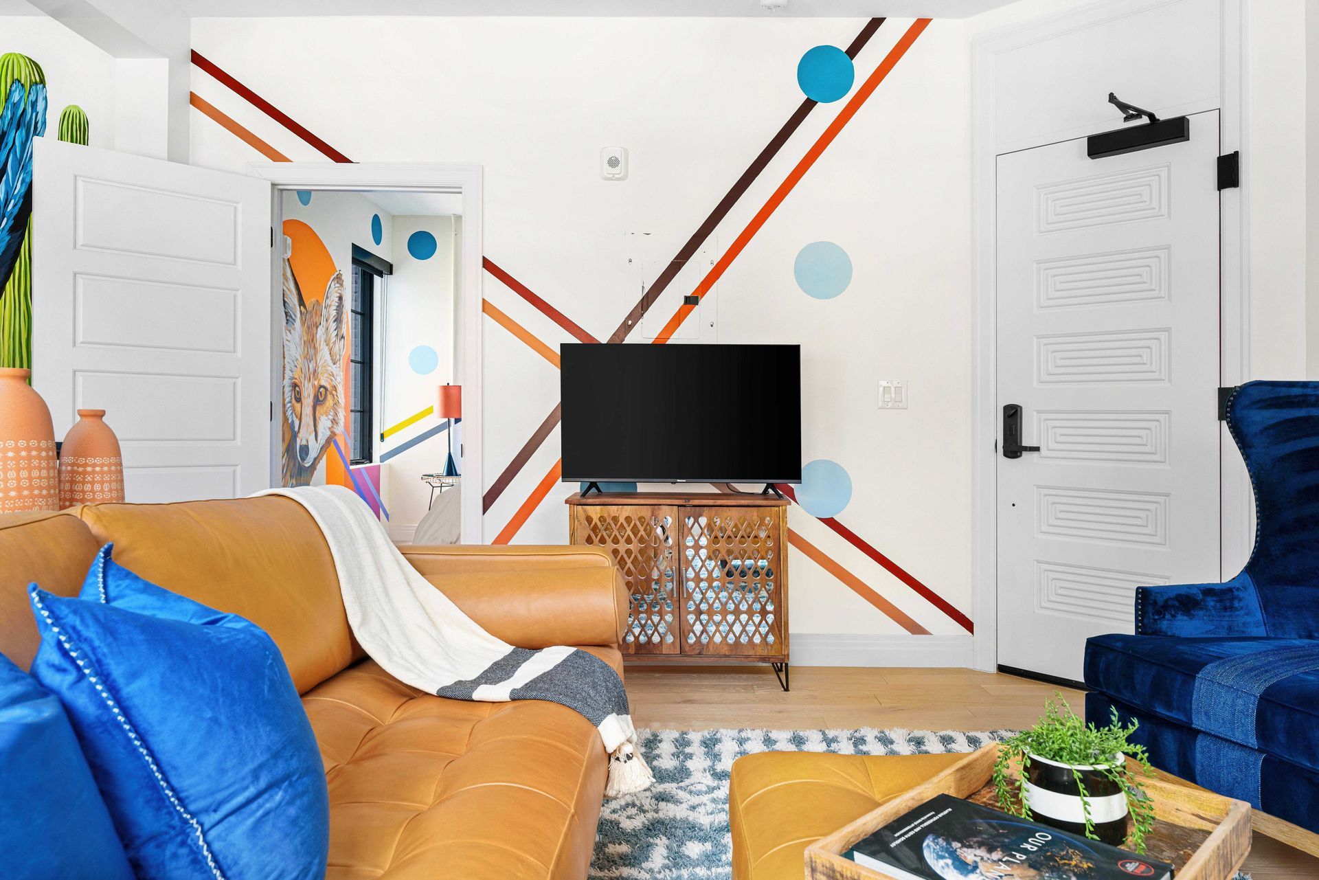 Bright living room with orange and blue sofas, TV, and wall art on a white accent wall